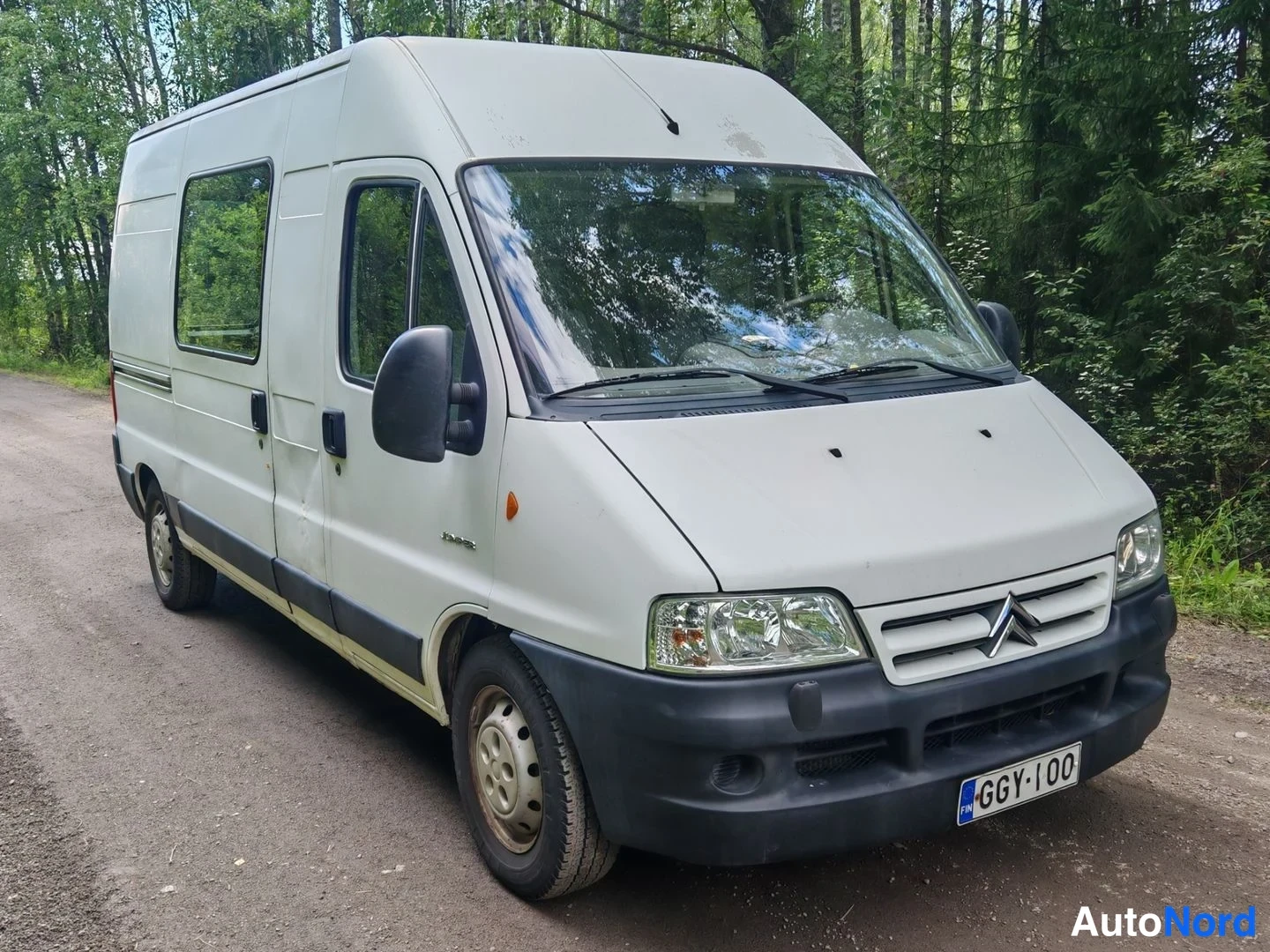 Etuviisto, nokka oikealle: Citroen Jumper -pakettiauto kolmesta neljänneksestä edestä oikealta valokuvaettuna, valkoinen korirakenne ja tumma etupuskuri metsätiellä.