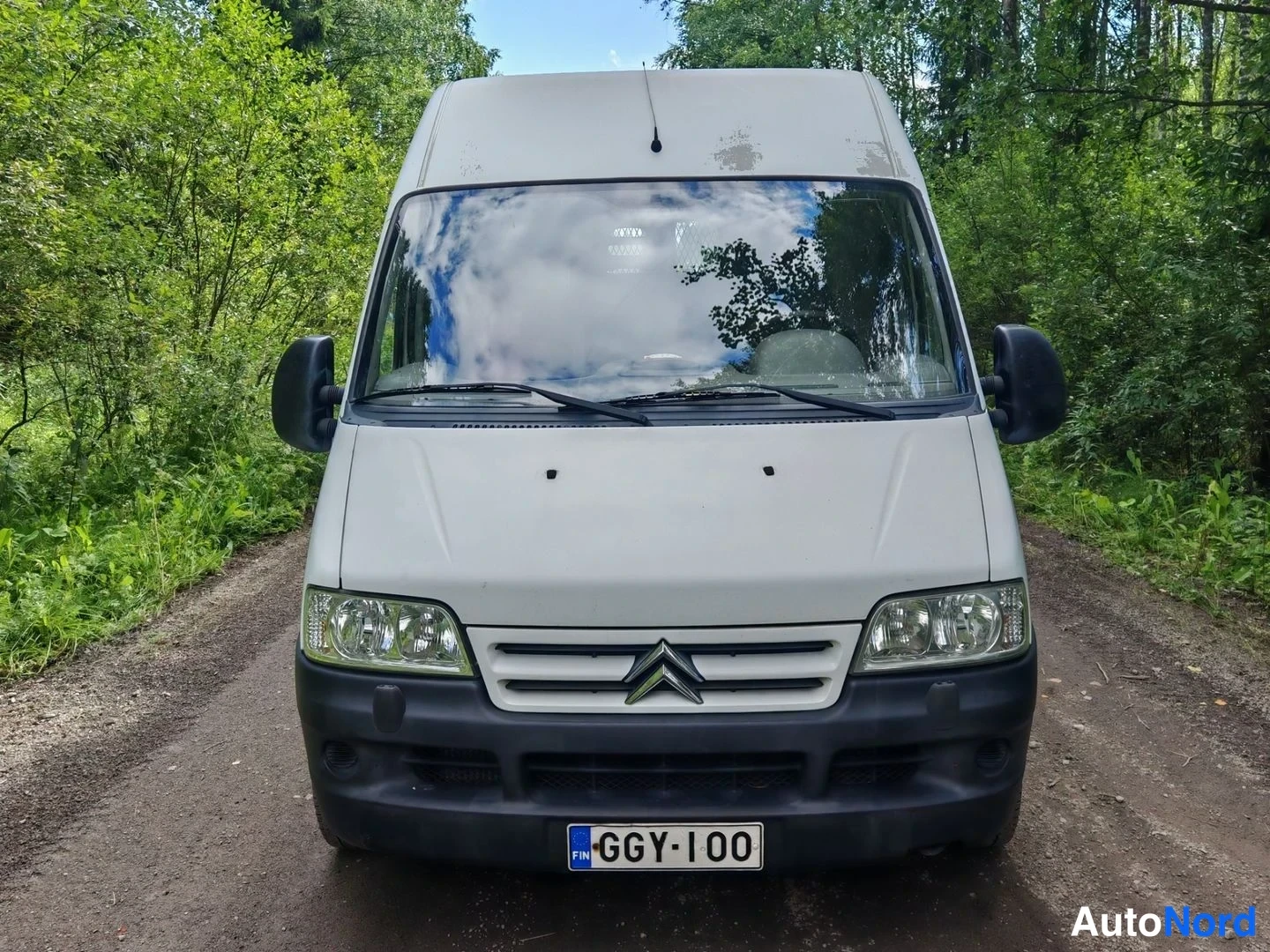Edestä: Citroen Jumper -pakettiauto suoraan edestä valokuvaettuna, valkoinen konepelti, Citroën-emblem ja rekisterikilpi.