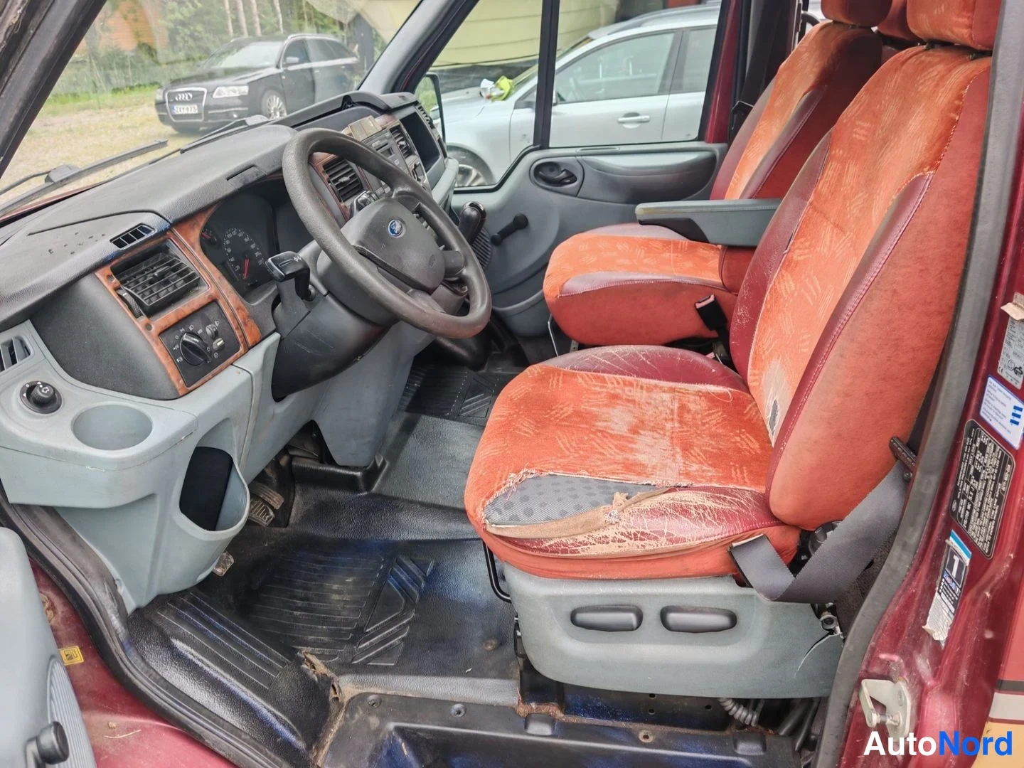 Muu: Ohjaamo kuljettajan puolelta: Ford-ohjauspyörä, mittaristo, kulunut punainen etuistuin ja lattiamatto.