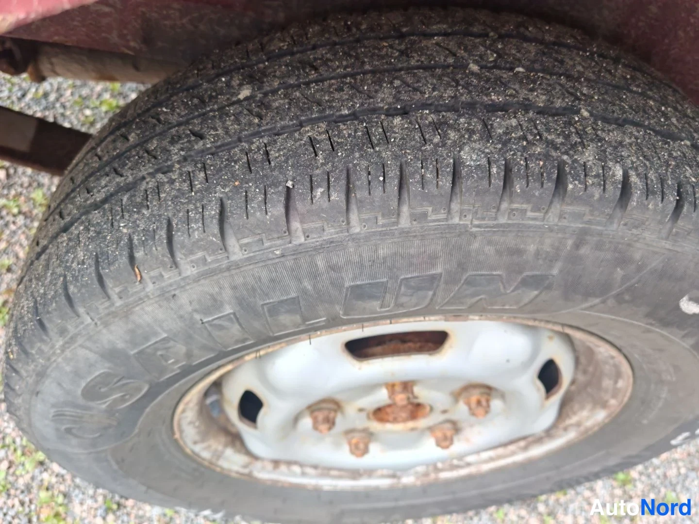 Yksityiskohta: Lähikuva auton renkaasta pölyisellä pintakulmalla ja valkoinen teräsvanne; renkaan sivussa osittain luettavissa teksti MICHELIN.