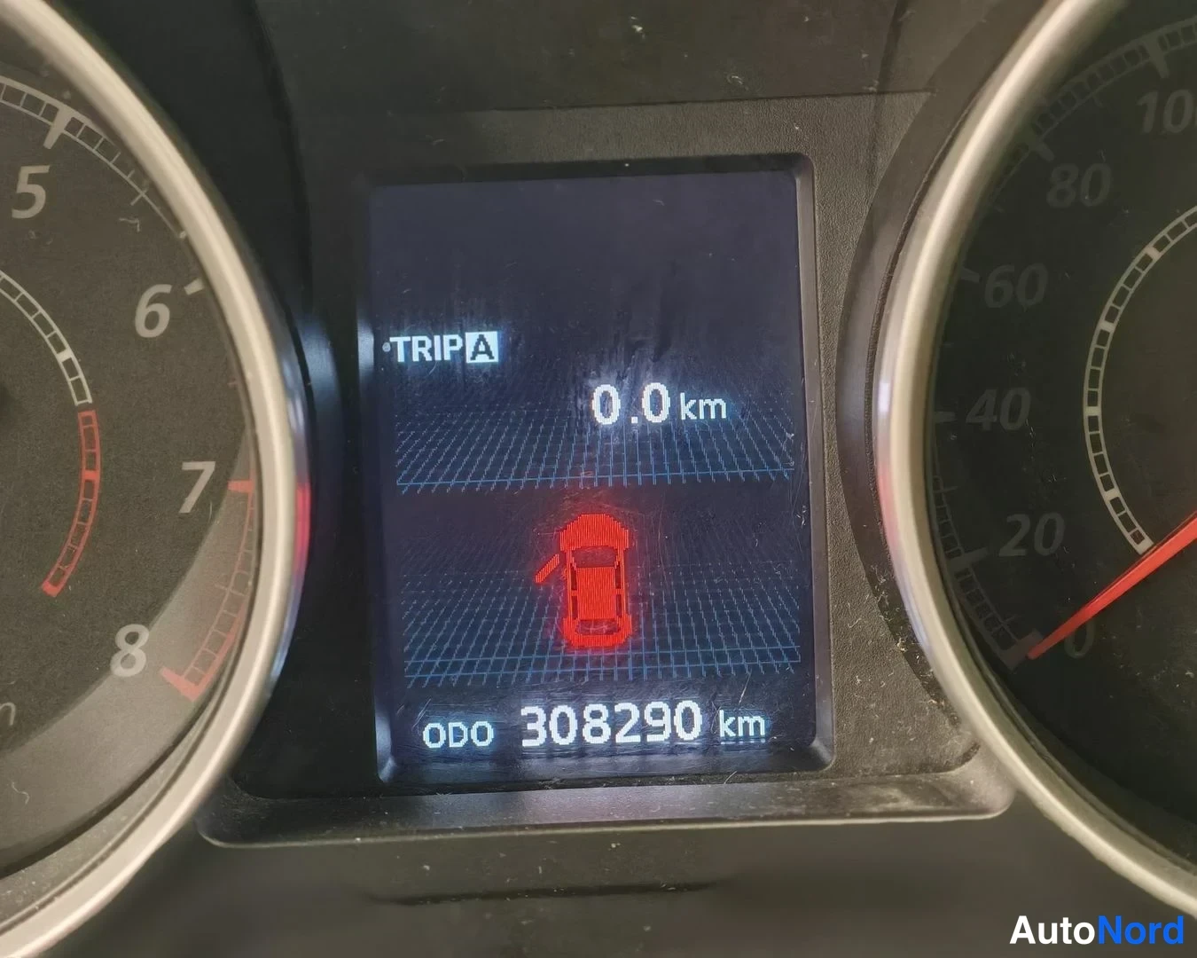 Sivulta: Kojeiston mittaristo lähikuvassa, ajotietonäyttö näyttää 'TRIP A 0.0 km' ja 'ODO 308290 km' sekä punaisen avoimen oven varoitusmerkin.