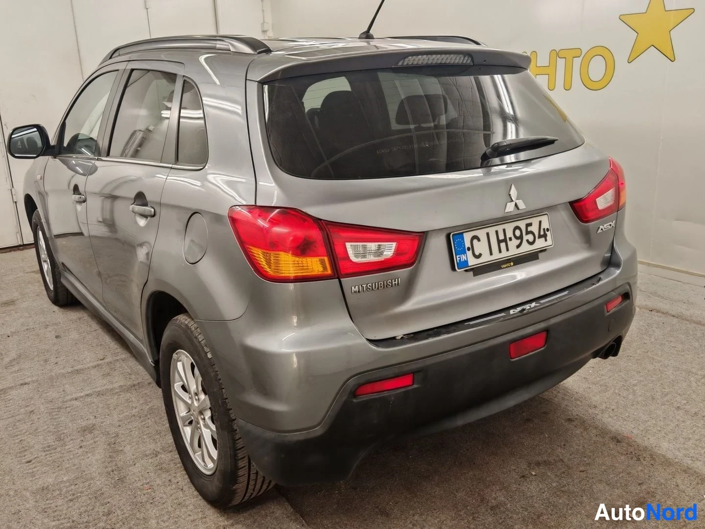 Takaviisto: Auton takaosa ja vasen kylki kolmesta neljänneksestä: hopeanharmaa Mitsubishi ASX, kattokaiteet, takavalot ja rekisterikilpi C1H-954 näkyvät.