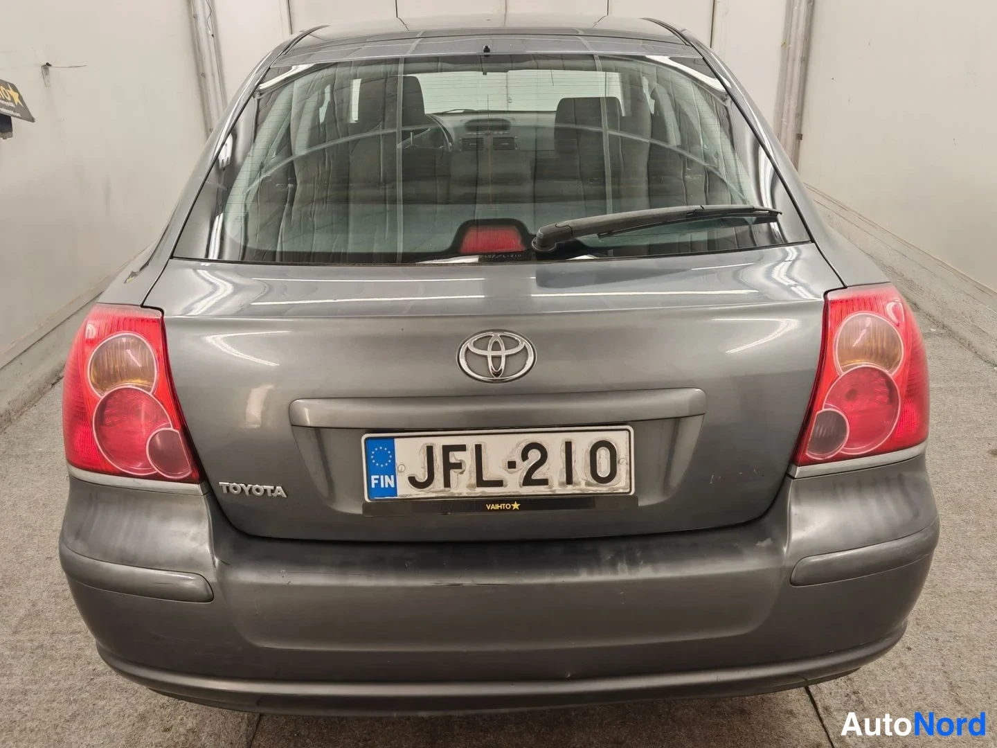 Takaa: Auton takapää suoraan takaa: harmaa Toyota, Toyota-merkki ja rekisterikilpi, punaiset takavalot ja takalasinpyyhkijä.