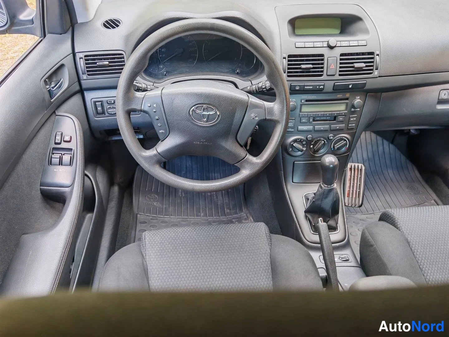 Muu: Ohjaamo mustilla penkeillä ja mattosarjalla, Toyota-ohjauspyörä, manuaalivaihteahje ja radio-lokero keskikonsolissa näkyvät etupenkiltä kuvattuna.
