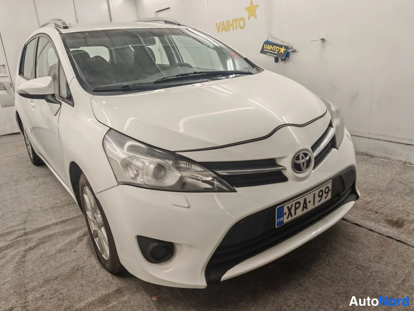Etuviisto, nokka oikealle: Toyotan etukulma oikealta: valkoinen koripaneeli, etusäleikkö ja Toyota-merkki, rekisteritunnus.