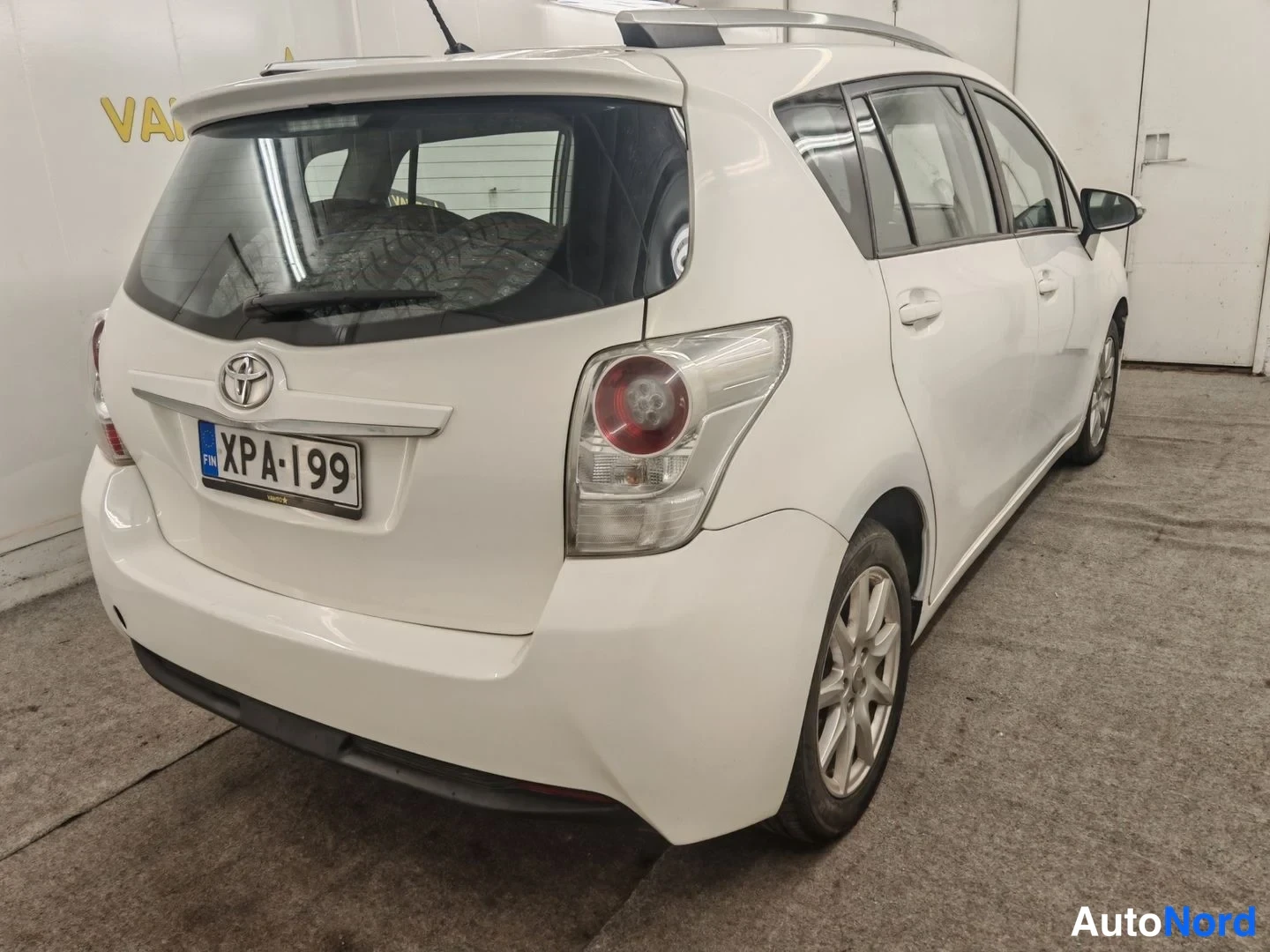 Takaviisto: Toyotan takaosa oikealta: valkoinen kori, takavalot ja Toyota-merkki, rekisteritunnus, kattokaiteet näkyvissä.