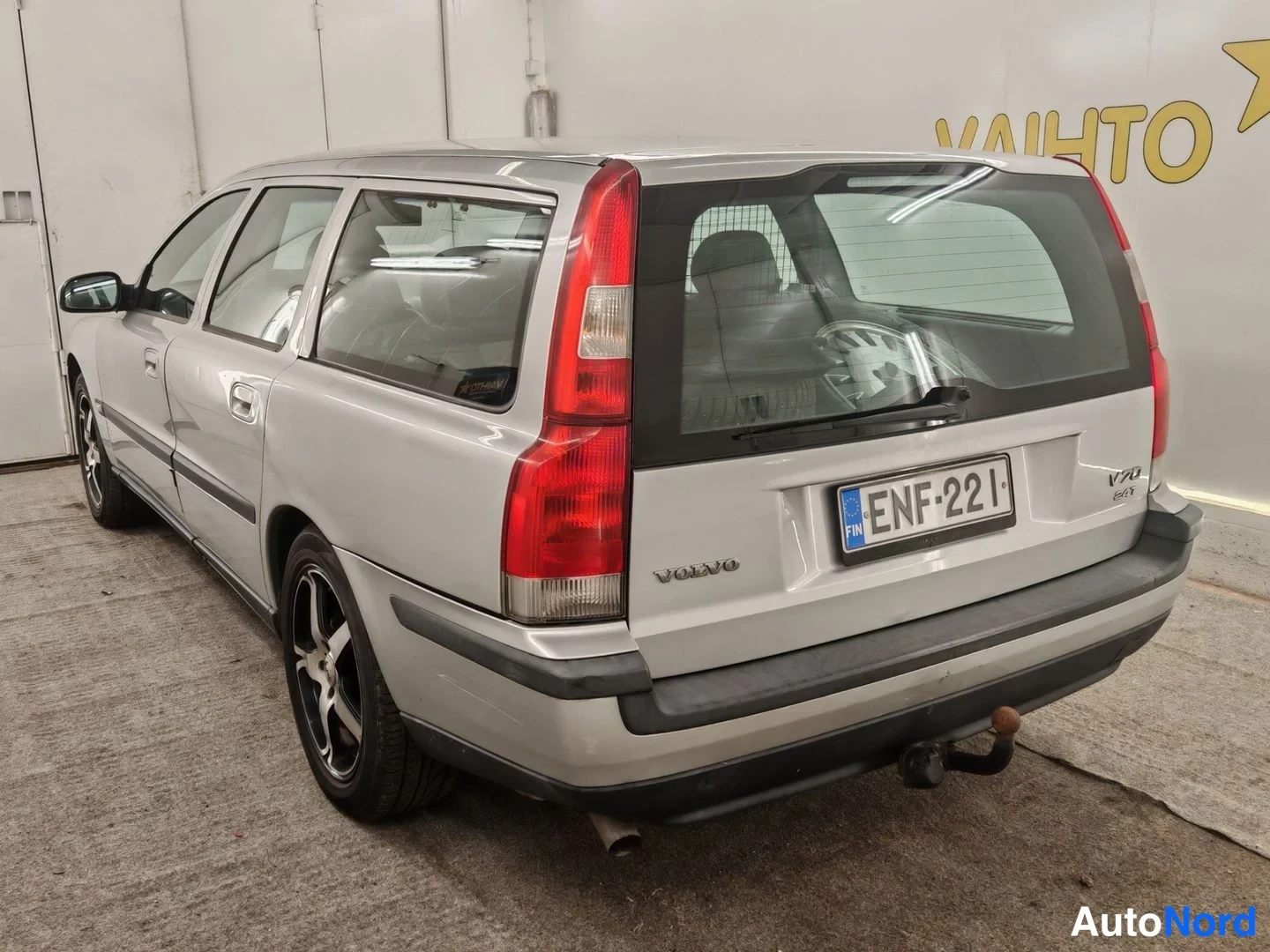 Takaviisto: Volvo V70 -farmari takaa vasemmalta kolmesta neljäsosasta, hopeanvärinen, takana vetokoukku ja rekisterikilpi.