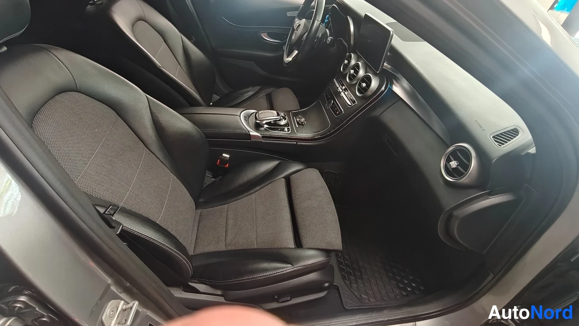 Muu: Ajetun Mercedes-Benz C -farmarin etusumu matkustamo: kaksi mustaa etuistuinta, keskikonsoli ja kojelauta näkyvät avatusta etiovesta.