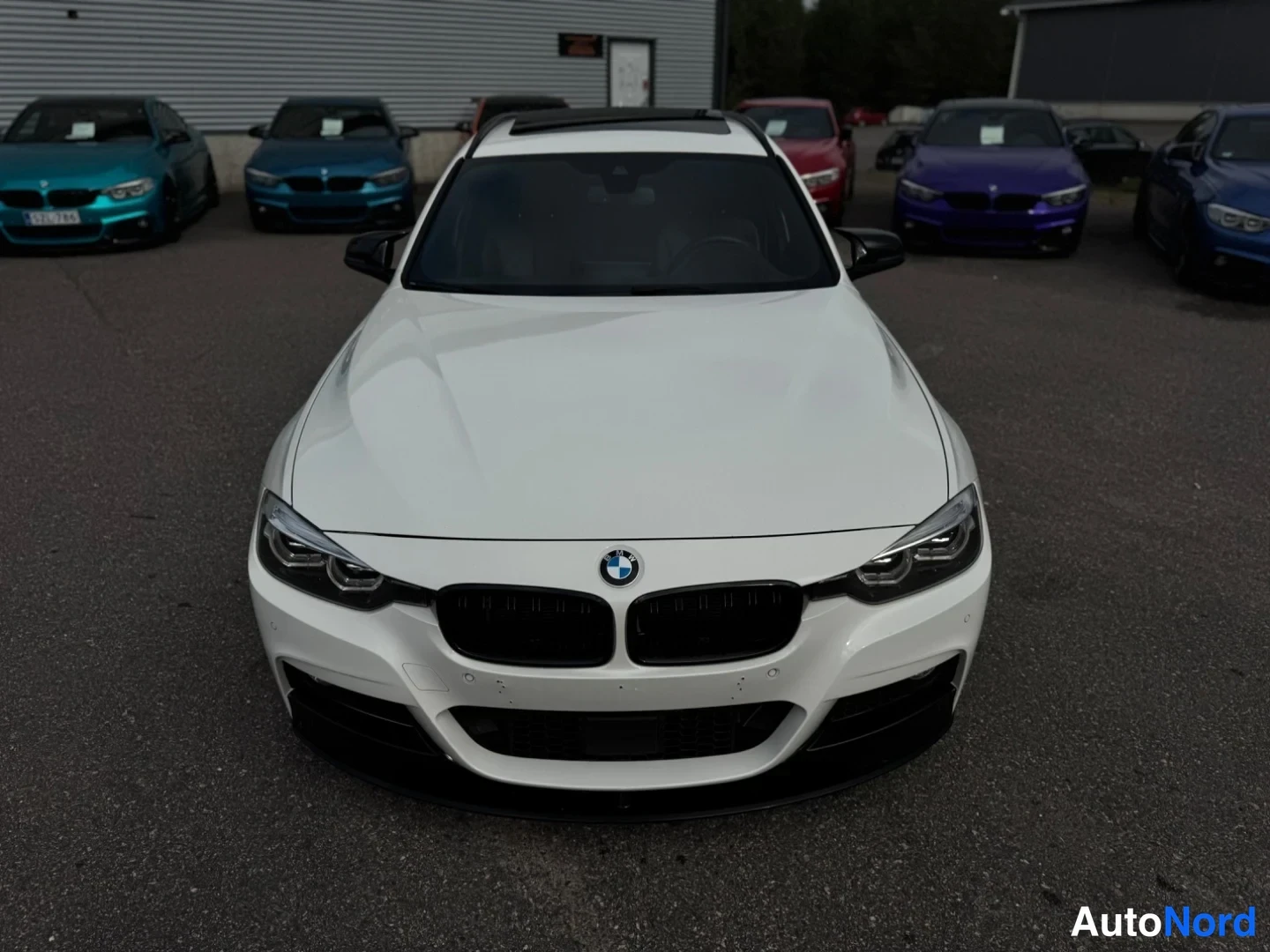 Edestä: BMW 3-sarja suoraan edestä valokuvattuna, valkoinen kori ja mustat etuspoilerit.