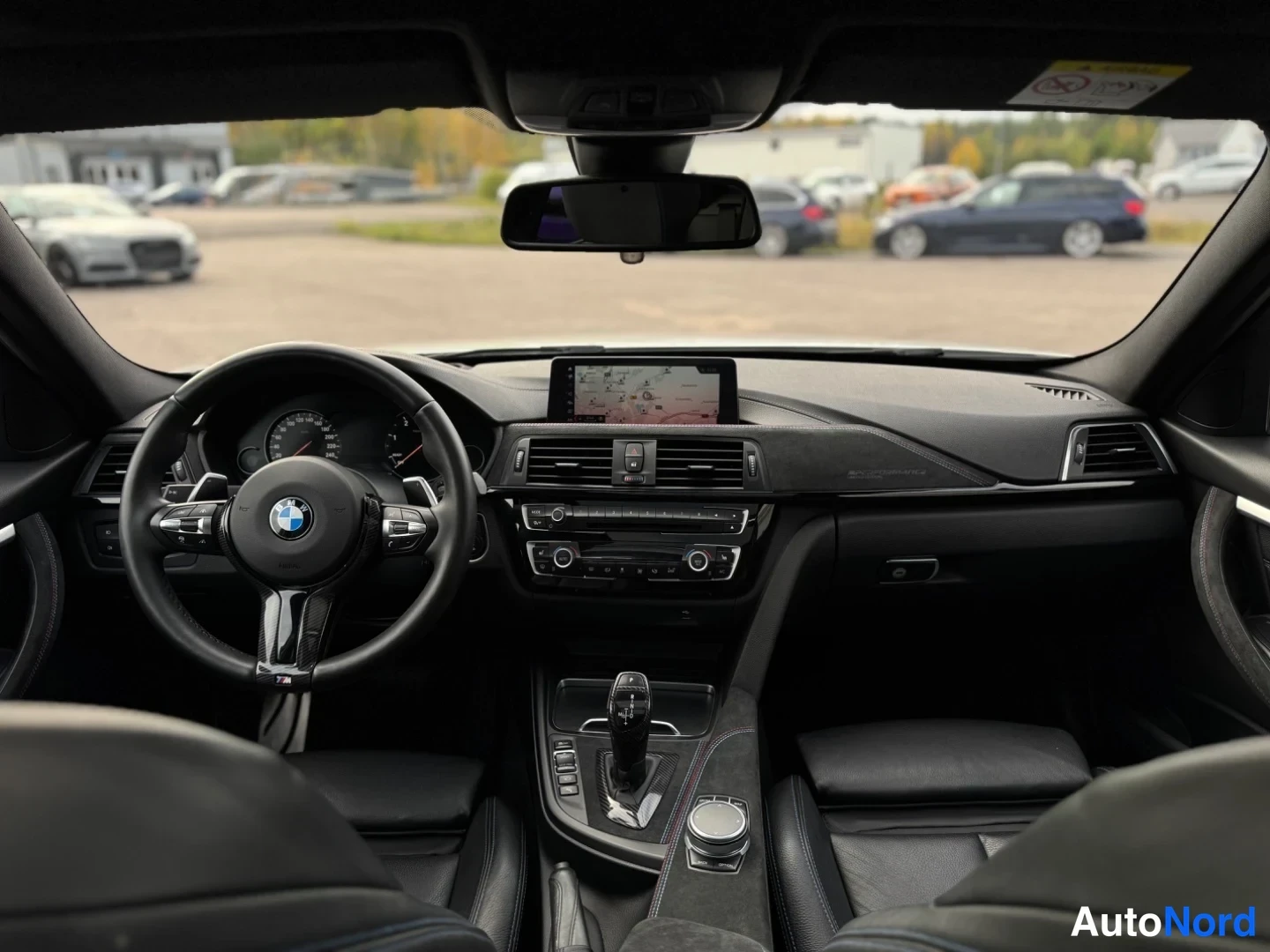 Yksityiskohta: Auton sisätilat etupenkeiltä kuvattuna: BMW-ohjauspyörä, kojelauta, karttaa näyttävä kesk töyttö, automaattivaihteen valitsin ja iDrive-ohjain.