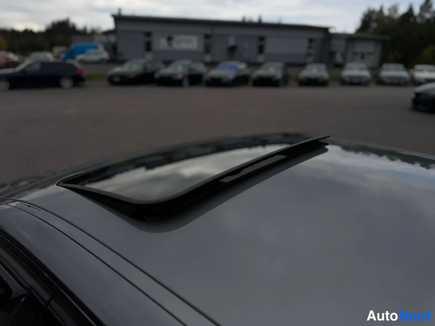 Sivulta: Lähikuva autokatolta: avattu kattoluukku, jonka nokka on ylhäällä, harmaa kattopaneeli heijastaa taivasta.