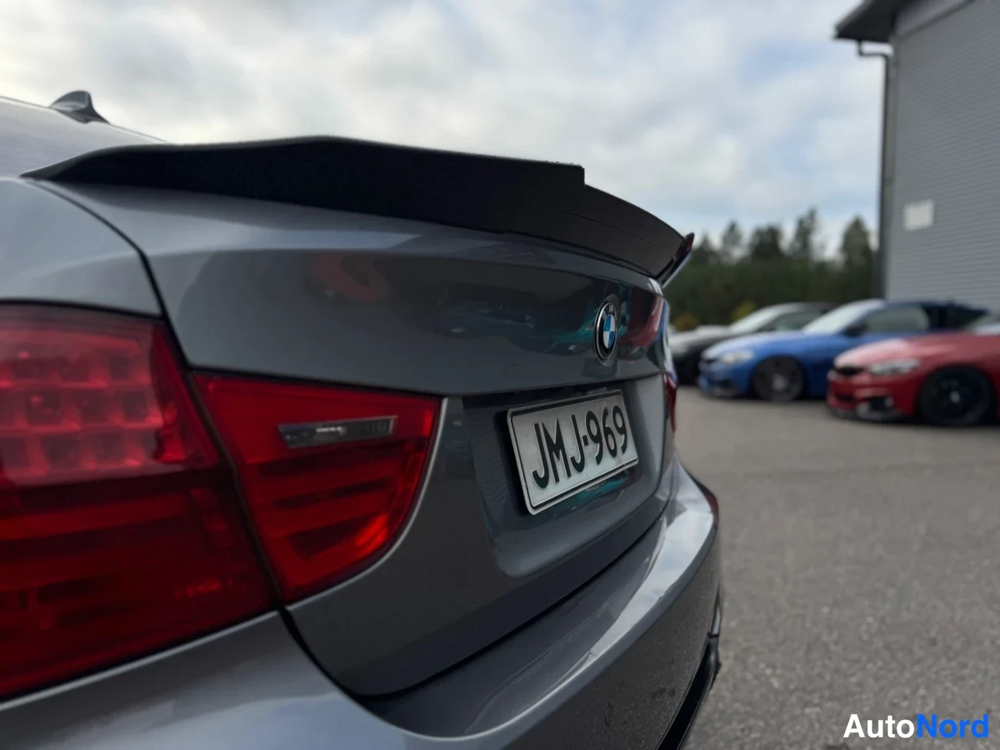 Takaa: Auton takapää: punainen takavalo, BMW-merkki, musta takaspoileri ja rekisterikilpi. Korin väri harmaa.