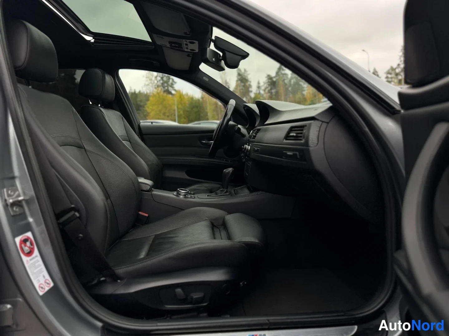 Etuviisto: Auton etusohva ja kojelauta ovelta katsottuna; mustat nahkaistuimet, panoraamikatto ja automaattivaihteen valitsin näkyvät.