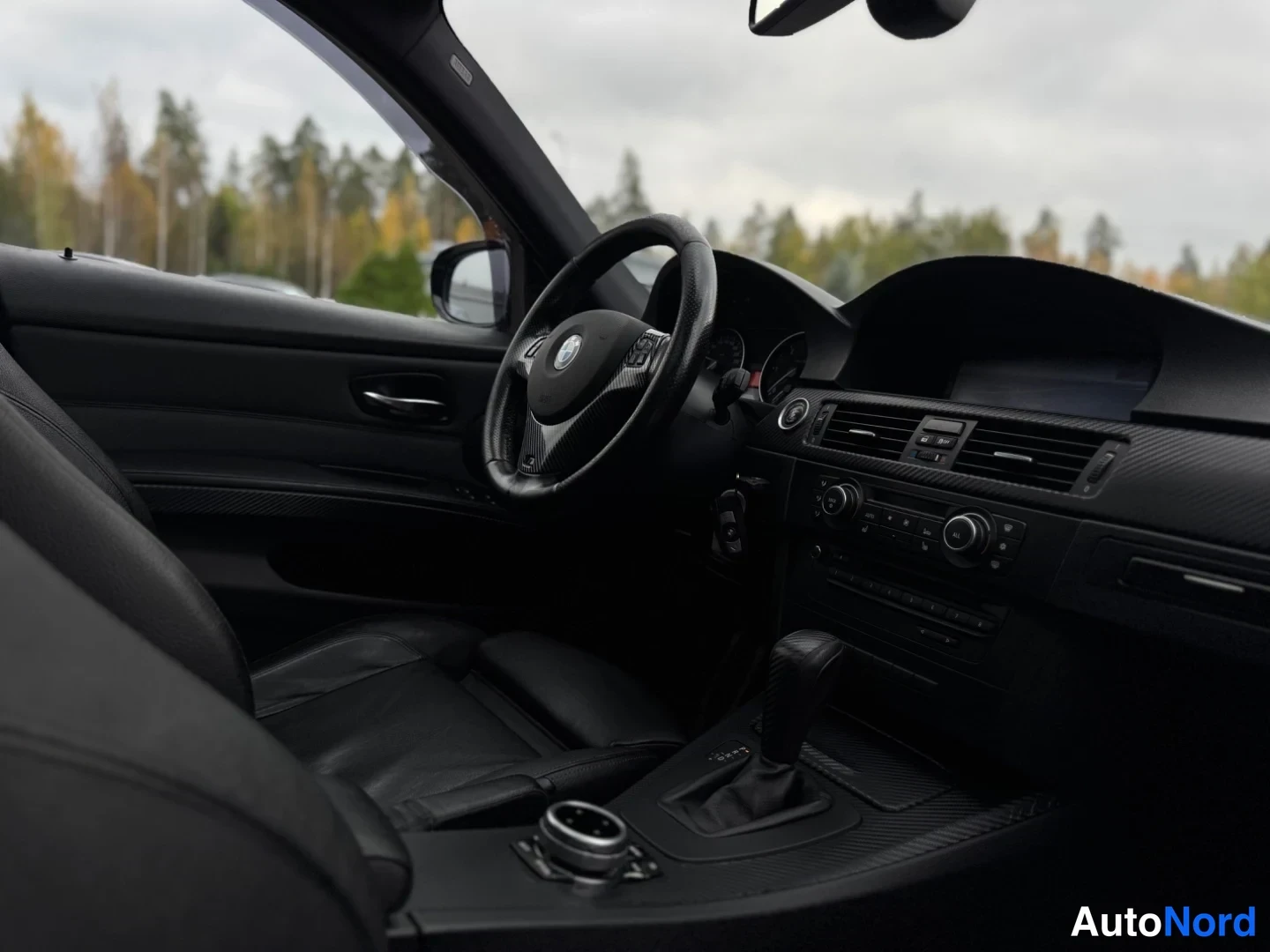 Etuviisto: Ohjaamo kuljettajan puolelta kuvattuna; BMW-ohjauspyörä,dashboard ja vaihteenvalitsin näkyvät.