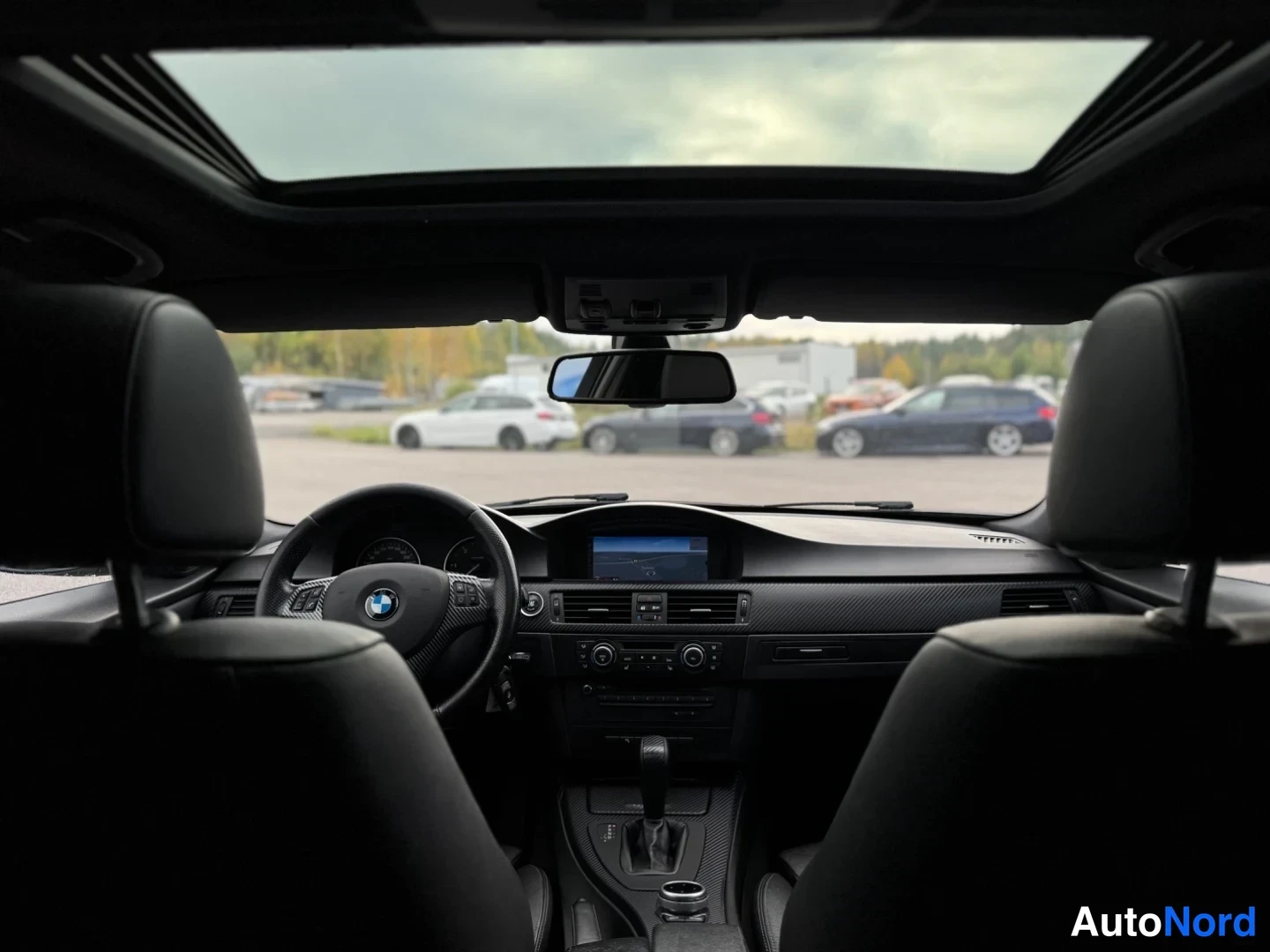Muu: Sisätila takaa päin: BMW-ohjauspyörä, tumma kojelauta, navigointinäyttö, automaattivaihteen valitsin ja avattava kattoluukku.