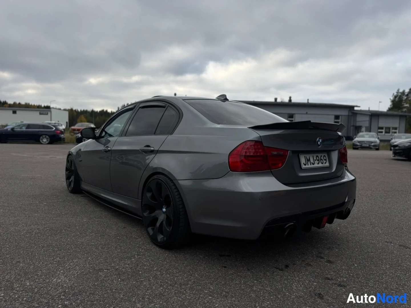 Takaviisto: BMW-sedan harmaana takaa oikealta kolmivartalokuvassa, musta spoileri, neljä pakoputkea ja -rekisterikilpi.