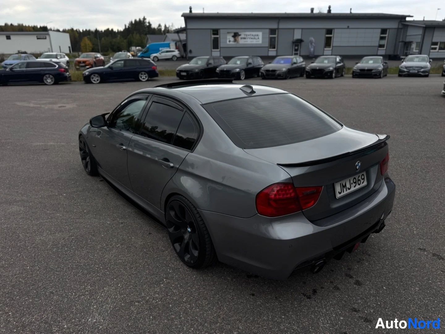 Takaviisto: BMW-sedan harmaana takaa vasemmalta kolmivartalokuvassa, musta spoileri ja mustat vanteet, -rekisterikilpi.