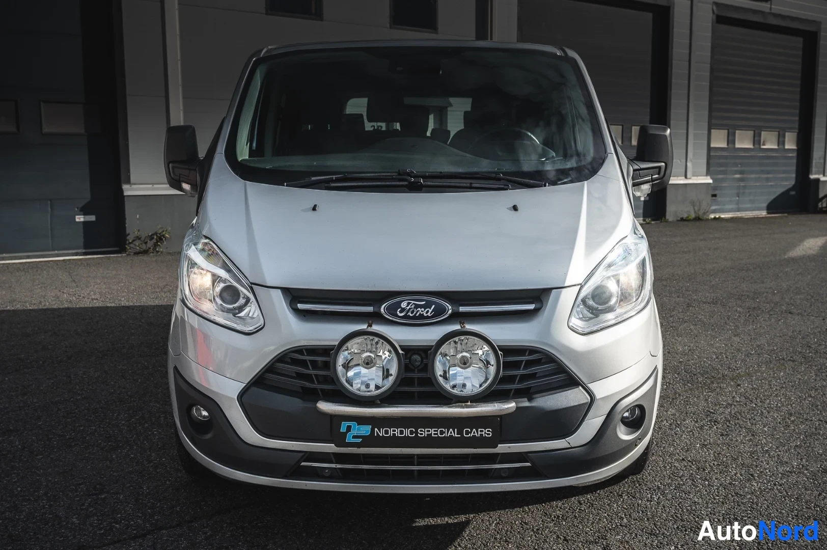 Edestä: Ford Tourneo Customin etunäkymä, hopea koripinta, kaksi lisävaloa etupuskurin yllä.