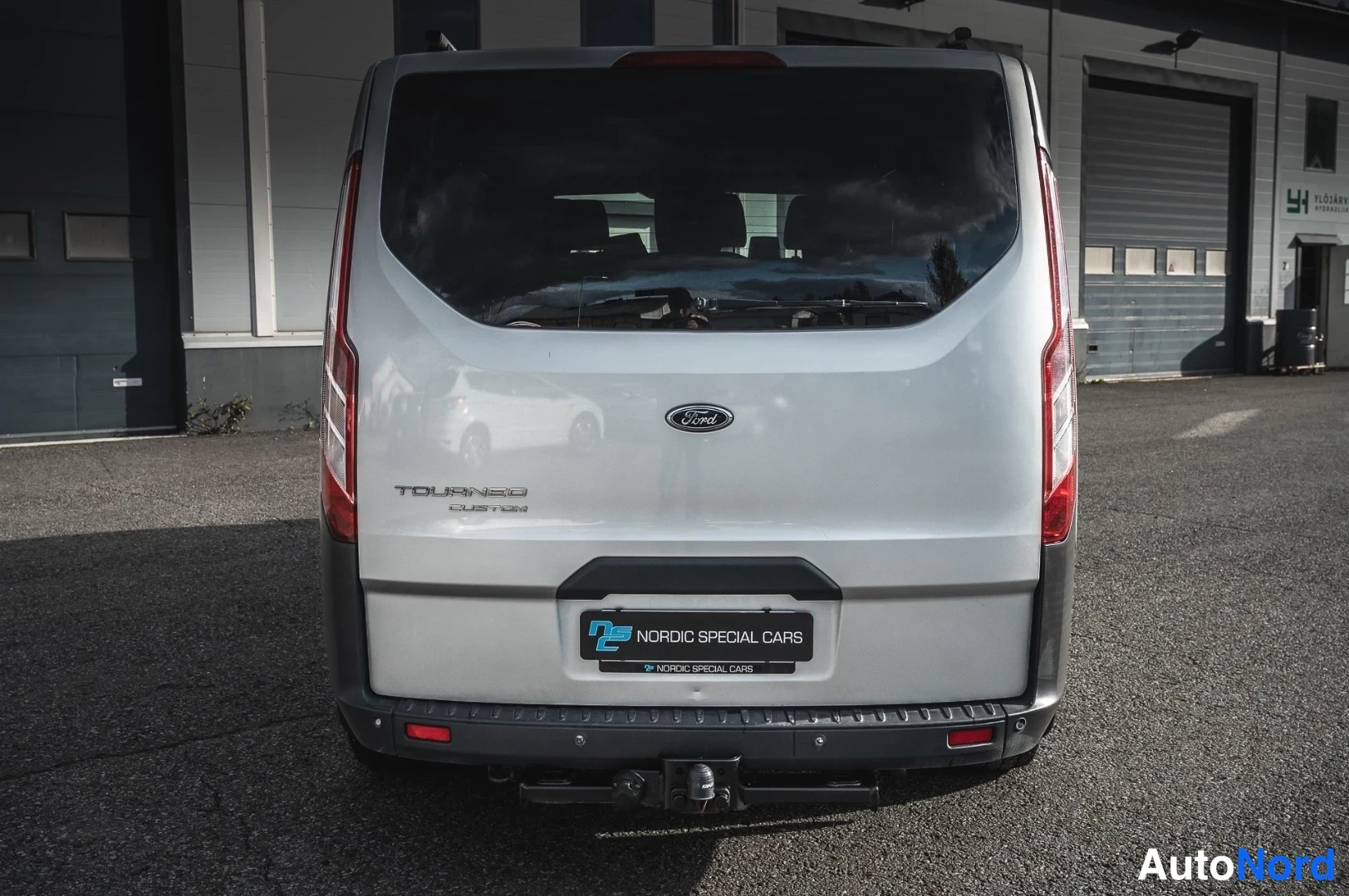 Takaa: Ford Tourneo Custom takaapäin, hopea koripinta, takavalot ja rekavetolaite näkyvissä.