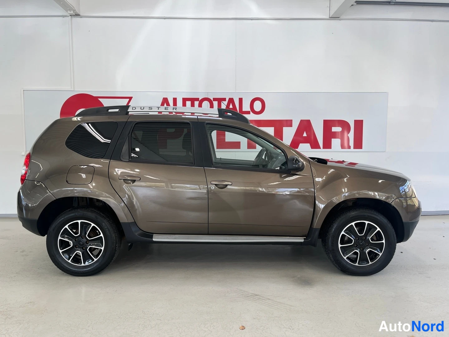 Sivulta: Sivukuva ruskeasta Dacia Duster -maasturista sisätiloissa, koko kylki näkyvissä.