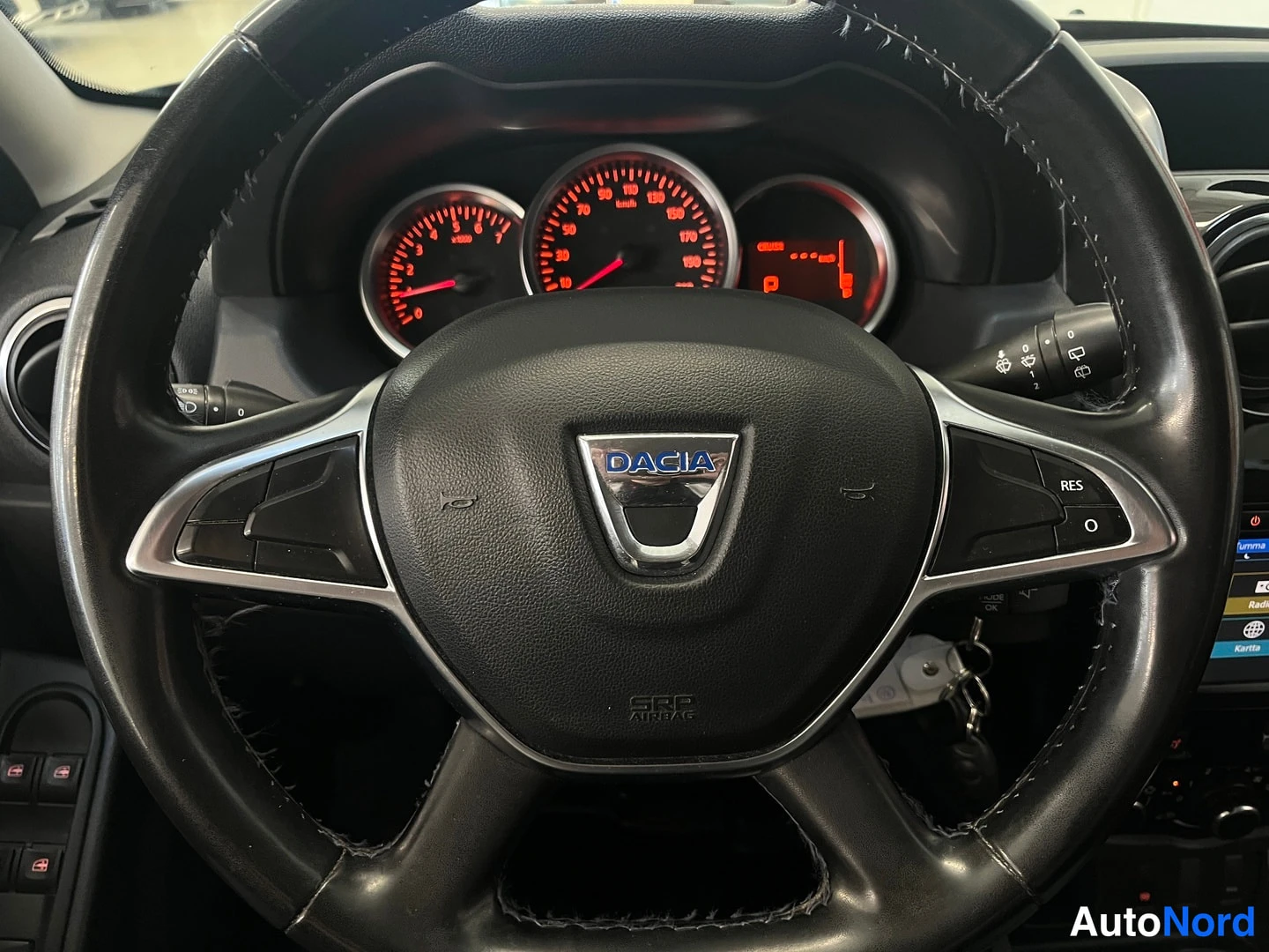 Muu: Dacia-ohjauspyörä lähikuvassa, mittaristo punaisin valaisin ja cruise control -painikkeet.