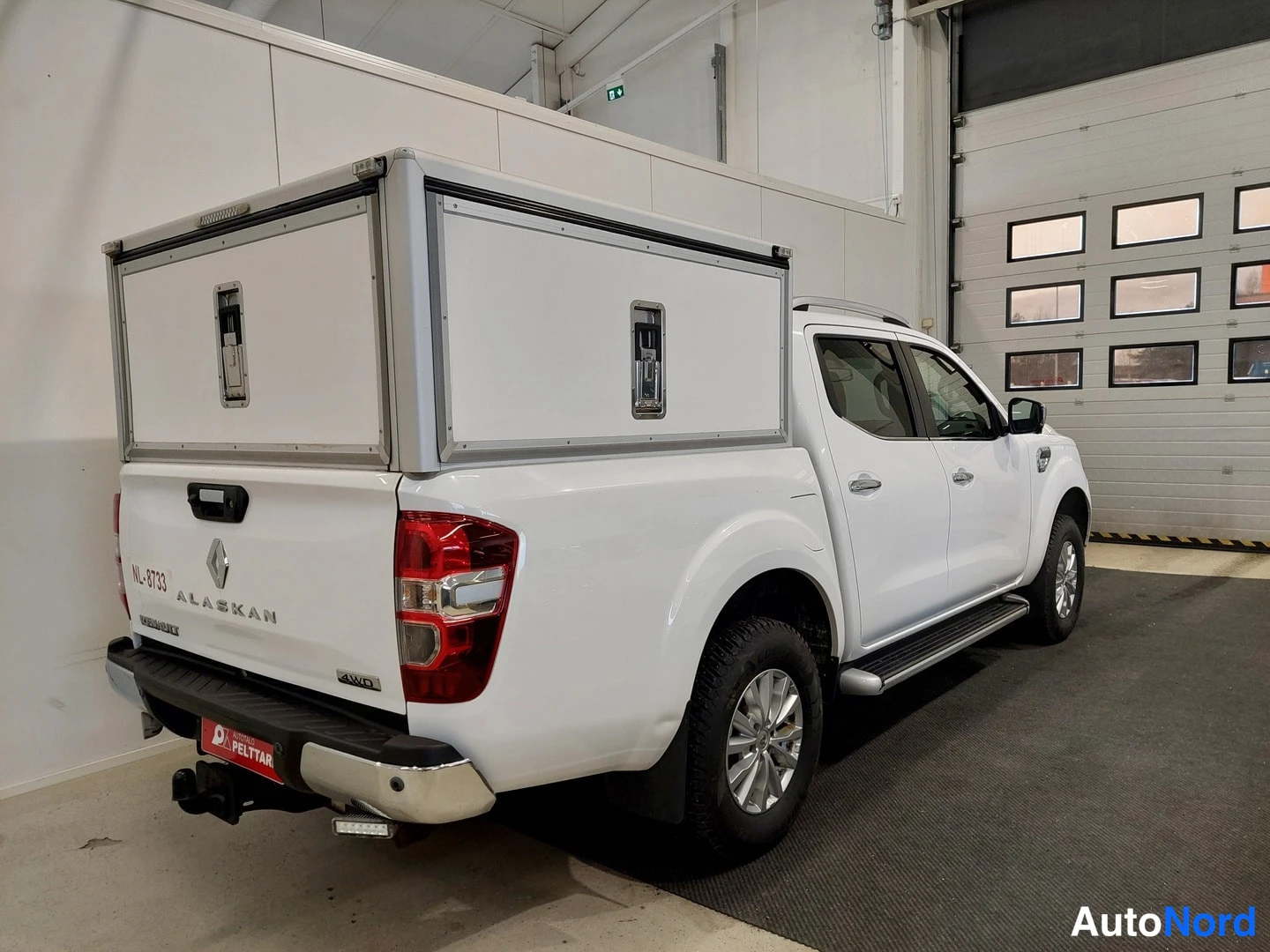 Takaviisto: Renault Alaskan -nottomalli takaa ja oikealta sivulta kuvattuna. Autossa valkoinen palvelulaatikko lavalla, rekisterikilpi NL-8733, ”4WD”-merkintä ja perävaunuk