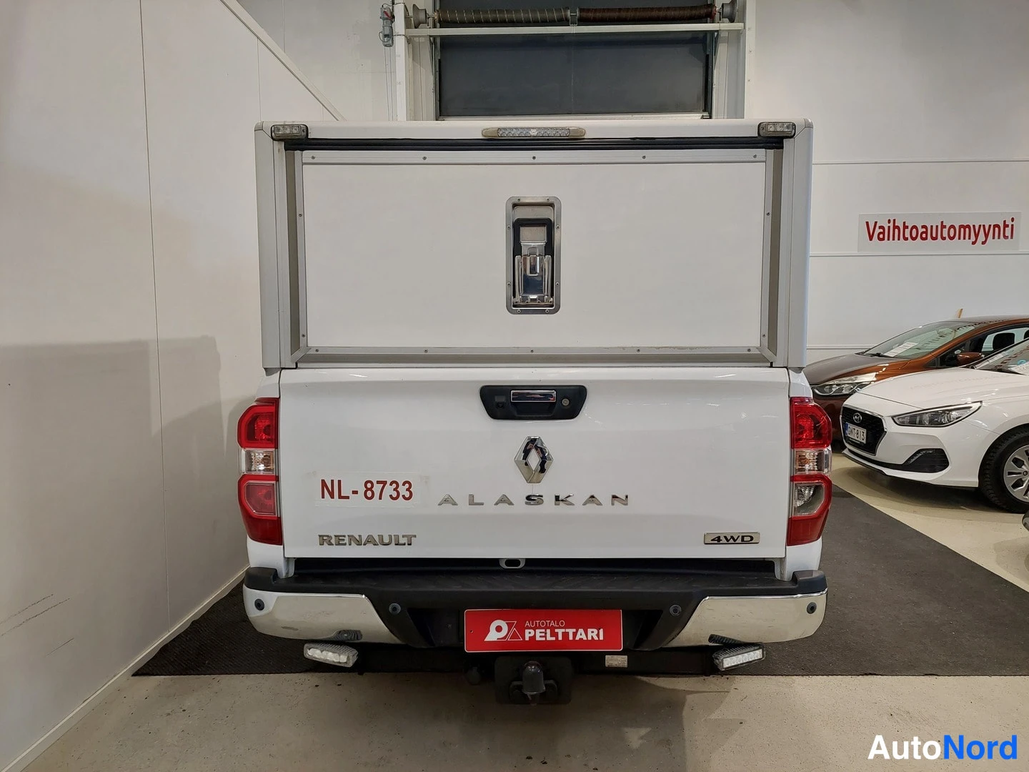 Takaa: Renault Alaskan -lava-auton takanäkymä sisätiloissa; takaluukussa rekisteri NL-8733, ALASKAN- ja RENAULT-tekstit sekä 4WD-merkintä, lavalla valkoinen säilytyska
