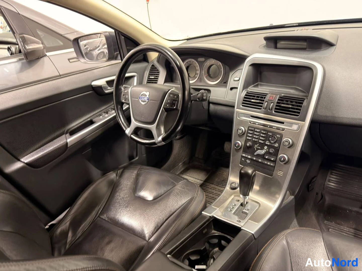 Muu: Volvo XC60:n etumatkustamon sisänäkymä: ohjauspyörä Volvo-logolla, mittaristo, keskikonsoli ja vaihdin.