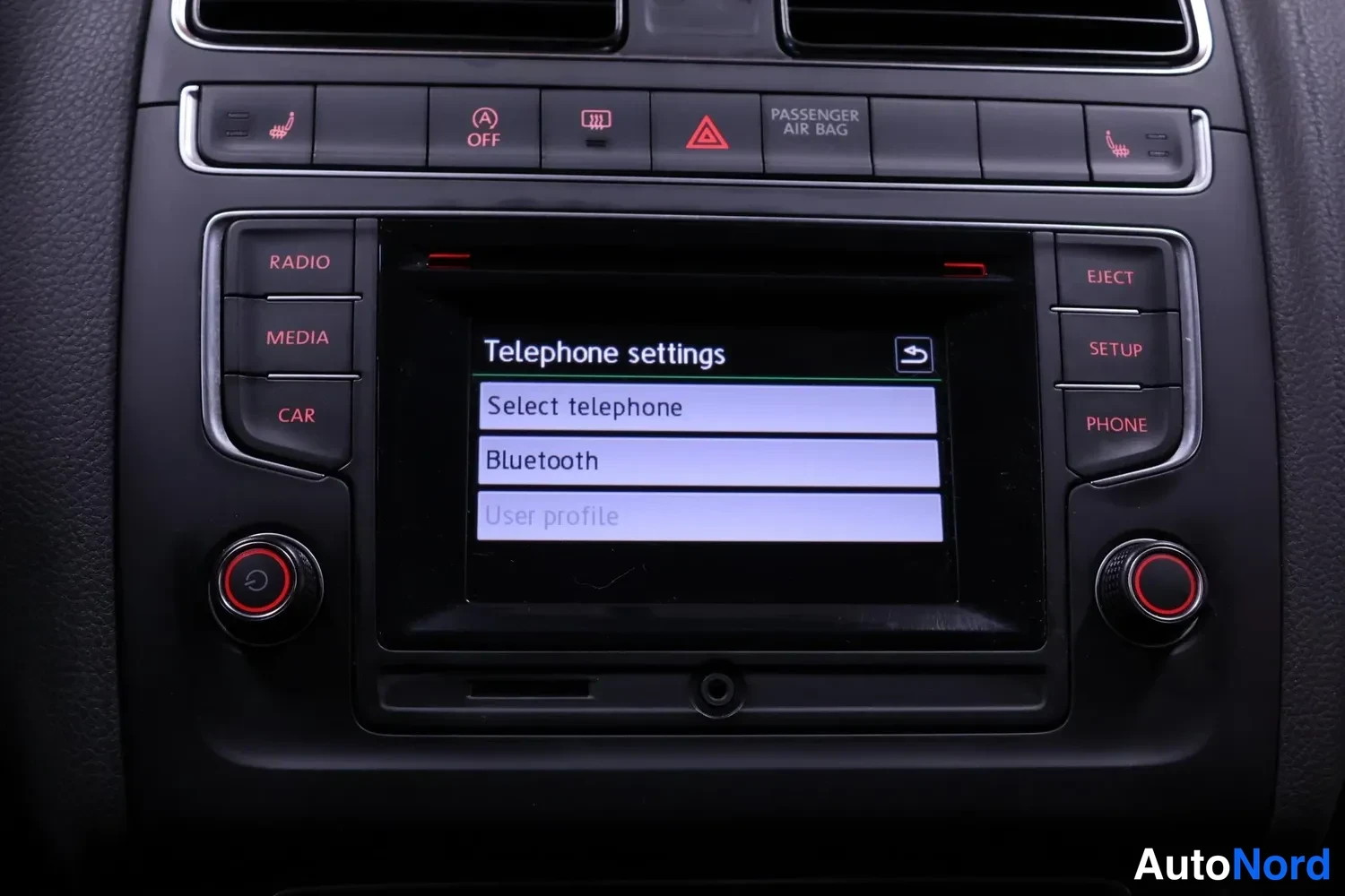 Edestä: Volkswagenin kojelaudan infotainment-näyttö, jossa on auki Telephone settings -valikko ja rivit Select telephone, Bluetooth ja User profile.