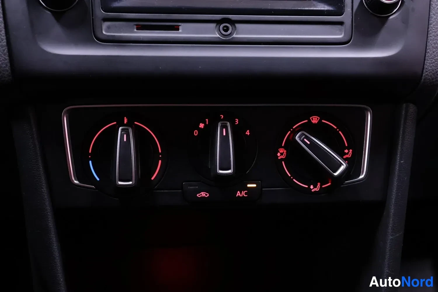 Edestä: Volkswagenin kojelaudan manuaalinen ilmastointipaneeli: kolme nuppia, A/C-painike valaistuna ja kierroslukunupin asemat 0–4.