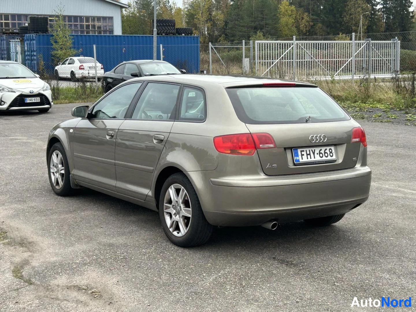 Takaviisto: Beige Audi A3 Sportback takakolmannelta vasemmalta näkyvä kuva, takavalojen ja rekisterikilven kanssa.