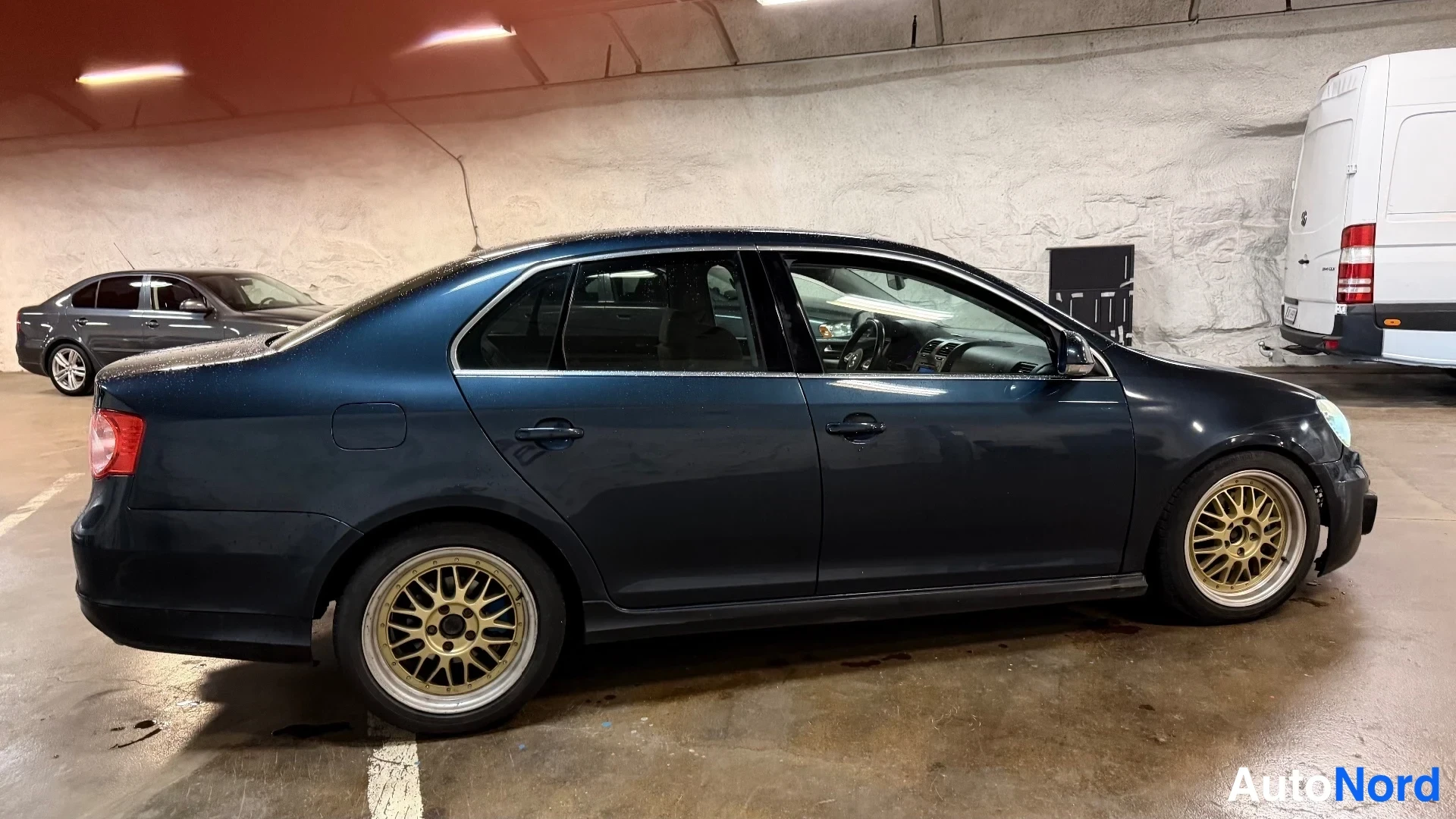 Takaviisto: Tummansininen Volkswagen Jetta -sedan takaviistosta, kultaväriset vanteet ja takavalot näkyvissä.