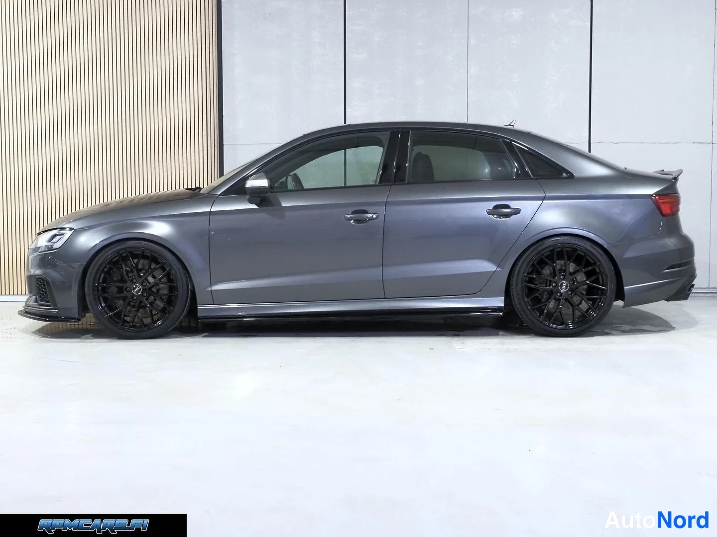 Sivulta: Harmaa Audi RS3 Sedan sivulta vasemmalta, mustat kevytmetallivanteet ja sivuhelat.