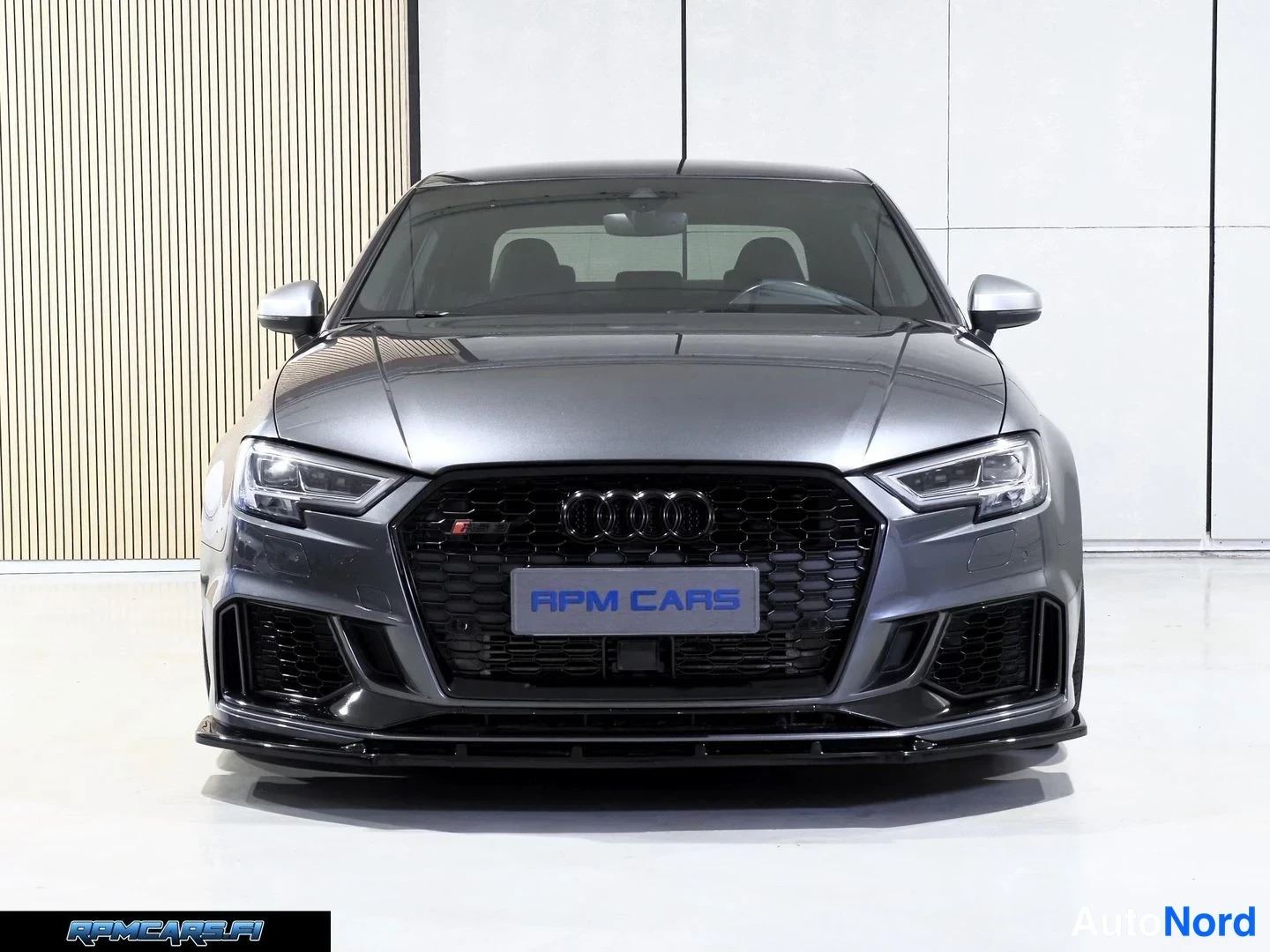 Edestä: Auton etupää suoraan edestä kuvattuna; Audi-monogrammi jäähdyttimen suojaverkossa, LED-ajovalot ja harmaa kori.