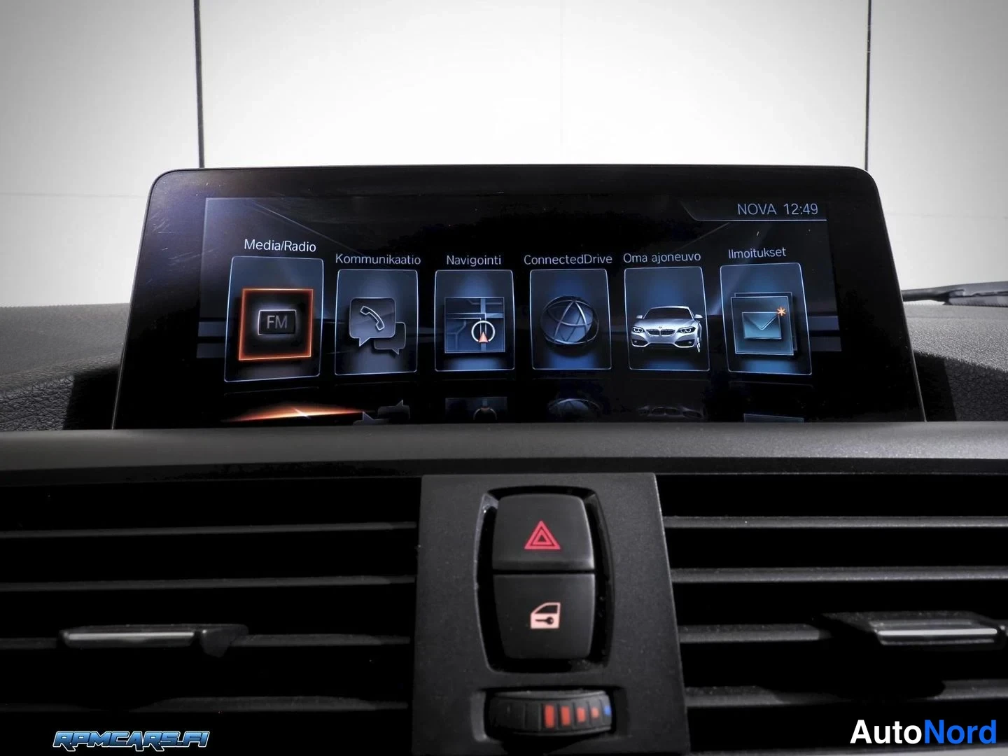 Yksityiskohta: Auton kojelaudan infotainment-näytön päävalikko valikkopainikkeilla Media/Radio, Kommunicaatio, Navigointi, ConnectedDrive, Oma ajoneuvo ja Ilmoitukset. Alla il