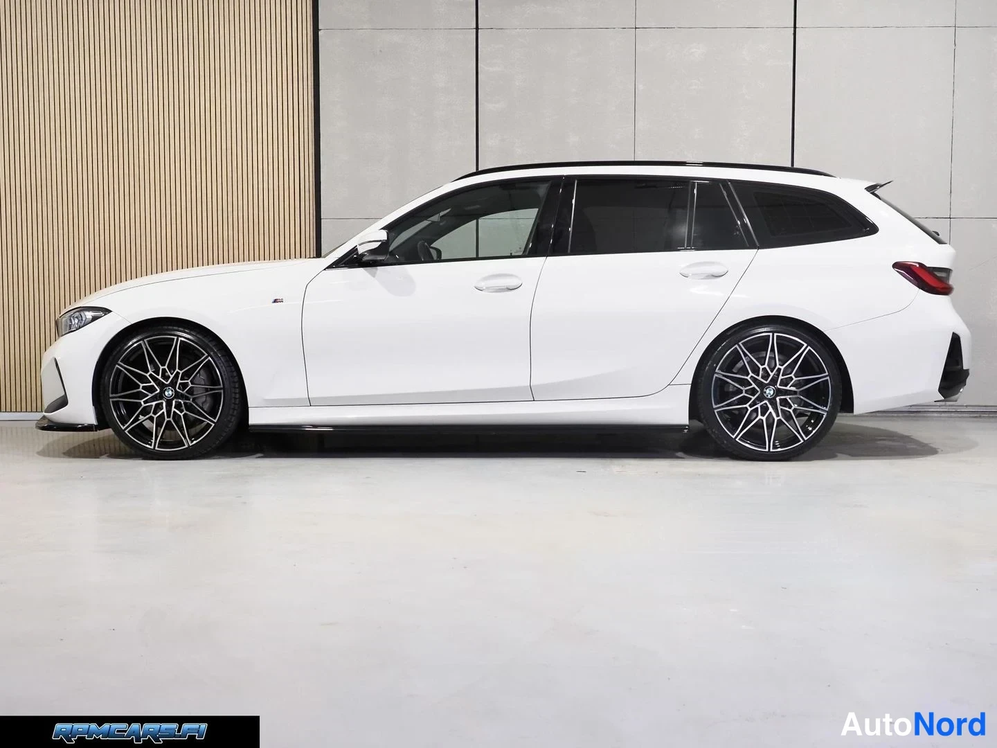 Sivulta: Valkoinen BMW Touring -farmari sivulta sisätiloissa, vasen sivu näkyy.