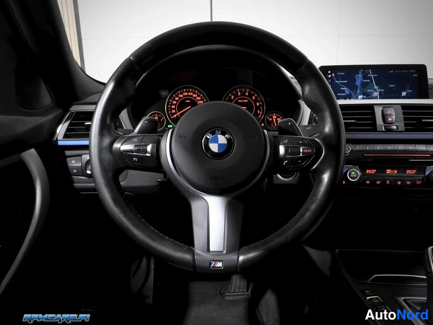 Muu: Ohjauspöytä BMW-ohjauspyörästä, jonka keskussa on BMW-embleemi ja alapuolella M-merkki; takana punaisilla mittareilla varustettu mittaristo, karttanäyttö ja kak