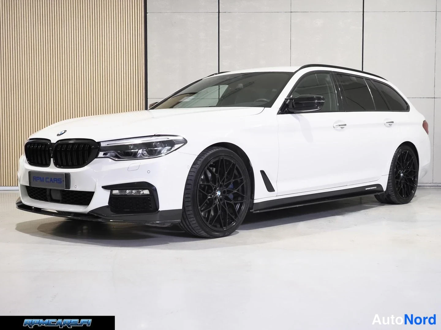 Etuviisto, nokka vasemmalle: BMW 5-sarjan farmari kolmeneljäsosan etukuvassa, valkoinen korimusta vanteilla sisätiloissa.