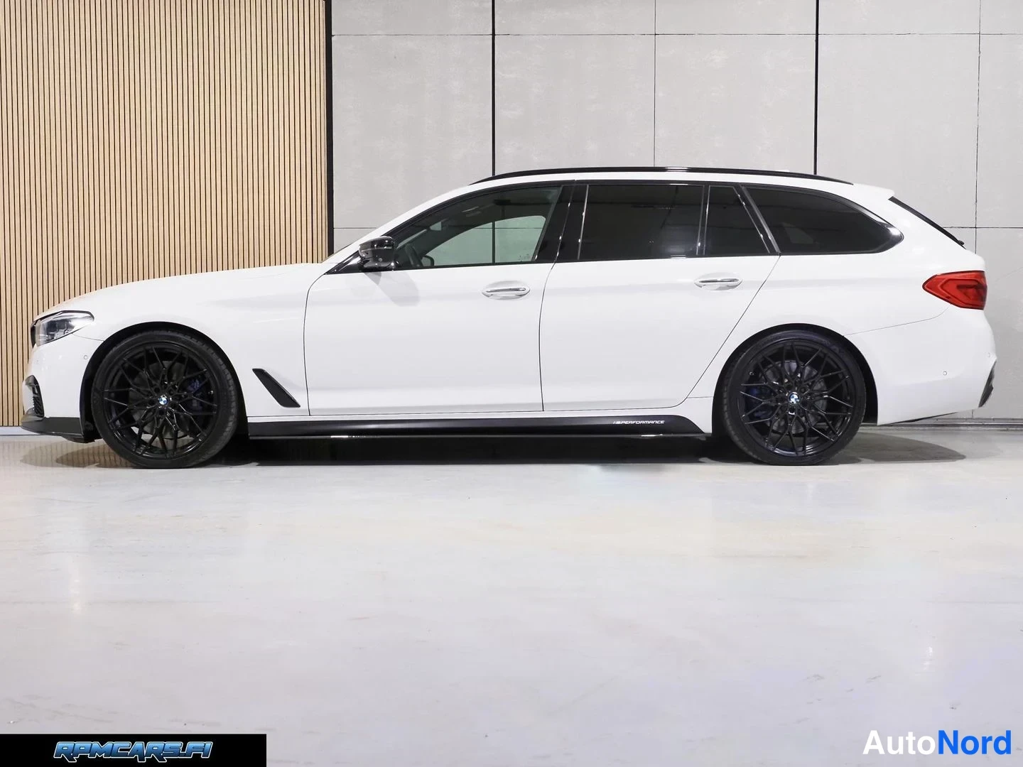 Etuviisto, nokka vasemmalle: BMW 5-sarjan farmarin sivukuva, valkoinen korimusta vanteilla sisätiloissa.
