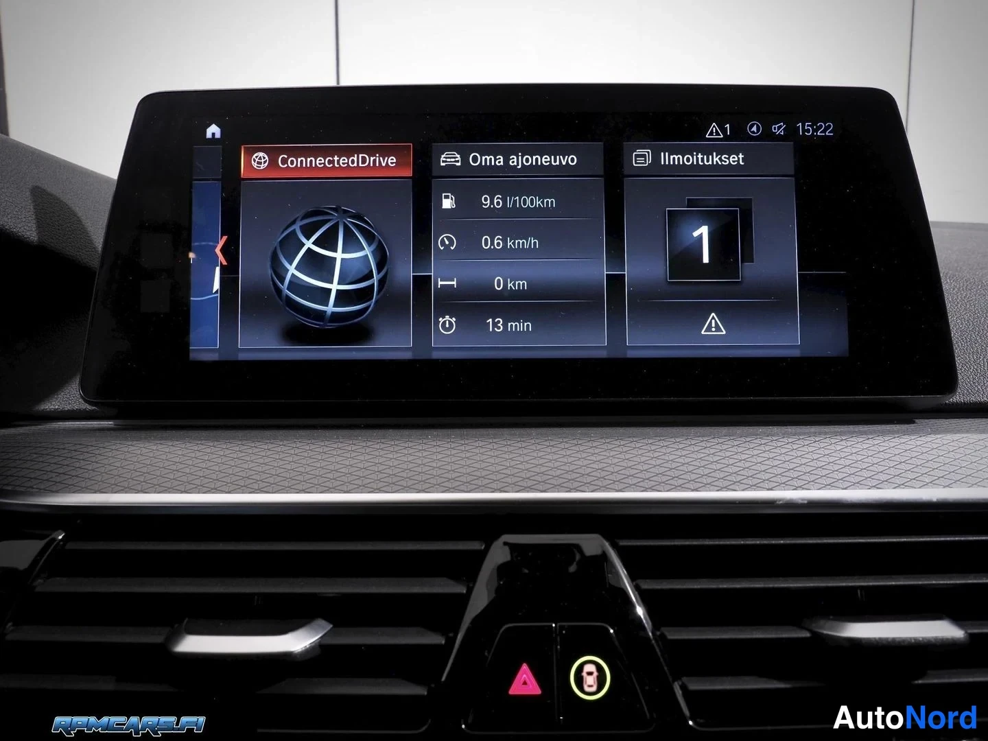 Sivulta: Infotainment-näyttö näyttää ConnectedDrive-valikon, Oma ajoneuvo -tiedot (9,6 l/100km, 0,6 km/h) ja Ilmoitukset-valikon.