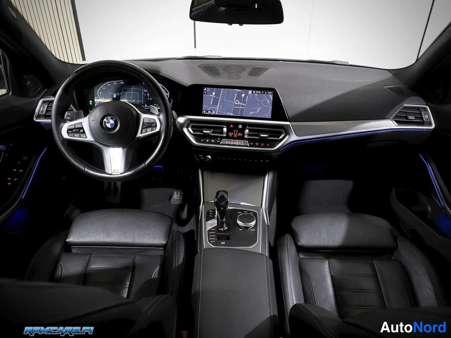 Edestä: Auton sisätila etupenkeiltä: musta ohjaamo, BMW-ohjauspyörä, digitaalinen mittaristo ja kartta näyttävä kosketusnäyttö keskikonsolissa, automaattivaihteen valit