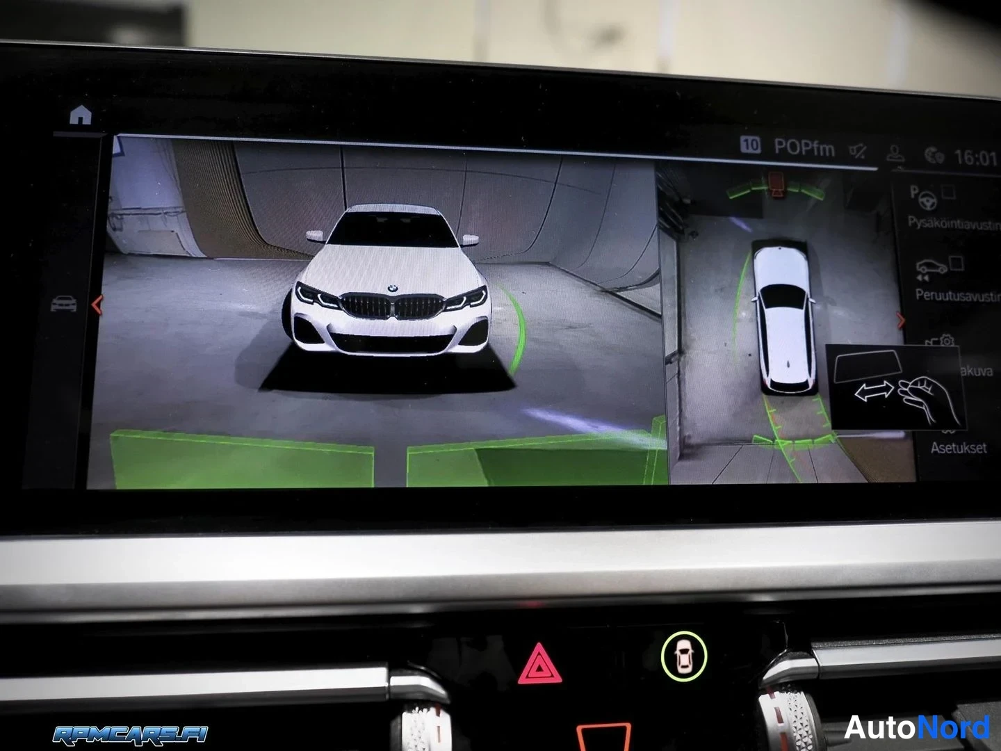 Yksityiskohta: Kojelaudan infotainment-näyttö näyttää 360-kameran kuvan valkoisesta autosta edestä ja ylhäältä, menettelystä kertovan kuvakkeen ja vihreät ohjeviivat. Edestä n