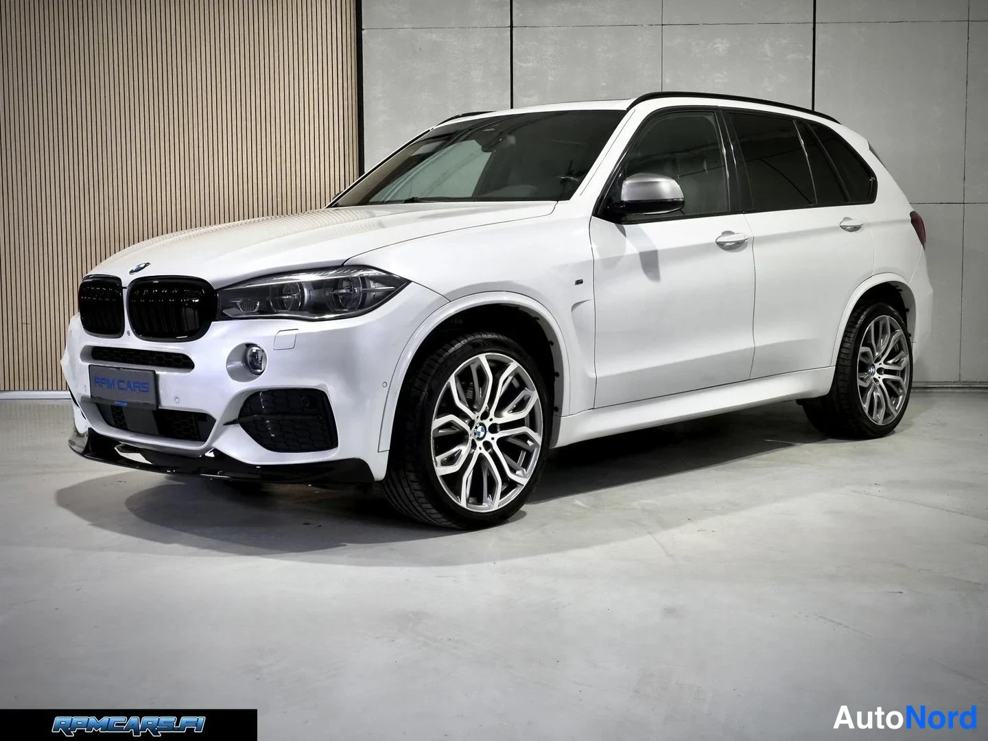 Etuviisto, nokka vasemmalle: Valkoinen BMW X5 -maastauto nähtynä etuviistosta studiossa, keulamaski ja edessä katkaistut LED-ajovalot näkyvät; vanteet ovat kaksiväriset kiiltävät.