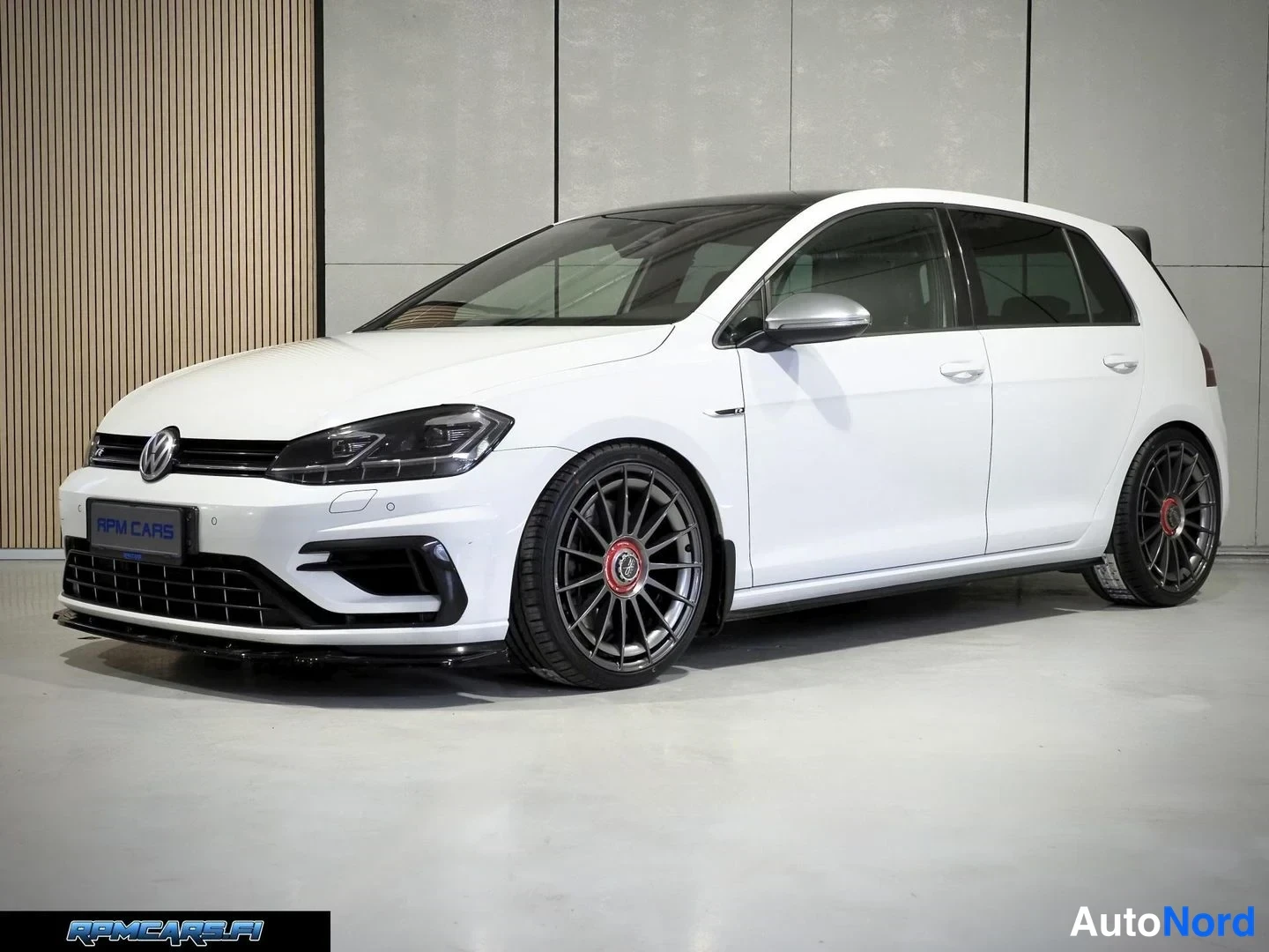 Etuviisto, nokka vasemmalle: Valkoinen Volkswagen Golf etukulmasta, tummat kevytmetallivanteet ja harmaa sisätila näkyvät.