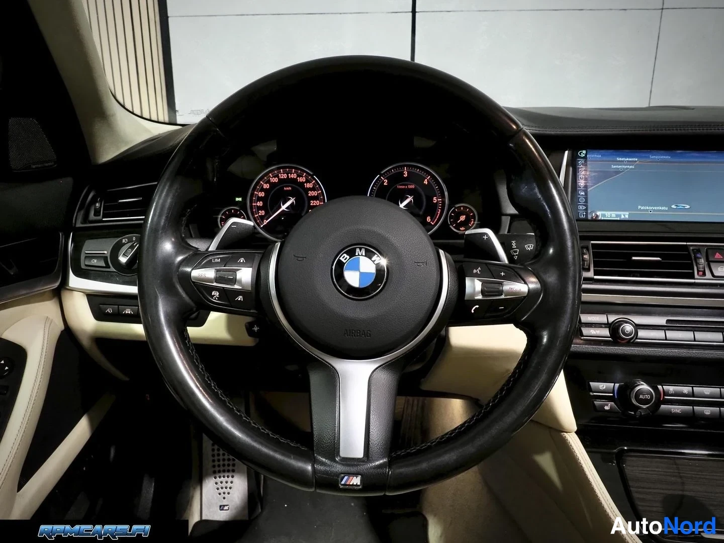 Muu: BMW-M-ohjauspyörä lähikuvassa, taustalla rustpunaisin merkkivain valaistut mittarit ja navigointinäkymä infotainment-ruudulla.