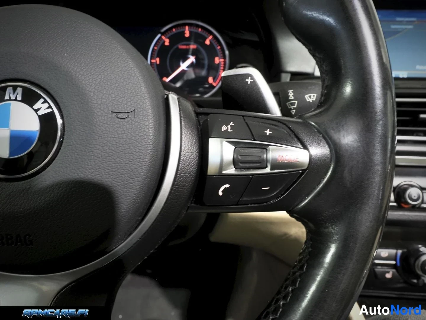 Muu: Lähikuva ohjauspyörän oikeasta pikanäppäinryhmästä: puhelin-, MODE- ja äänenvoimakkuuspainikkeet, taustalla mittaristo ja infotainment-ruutu.