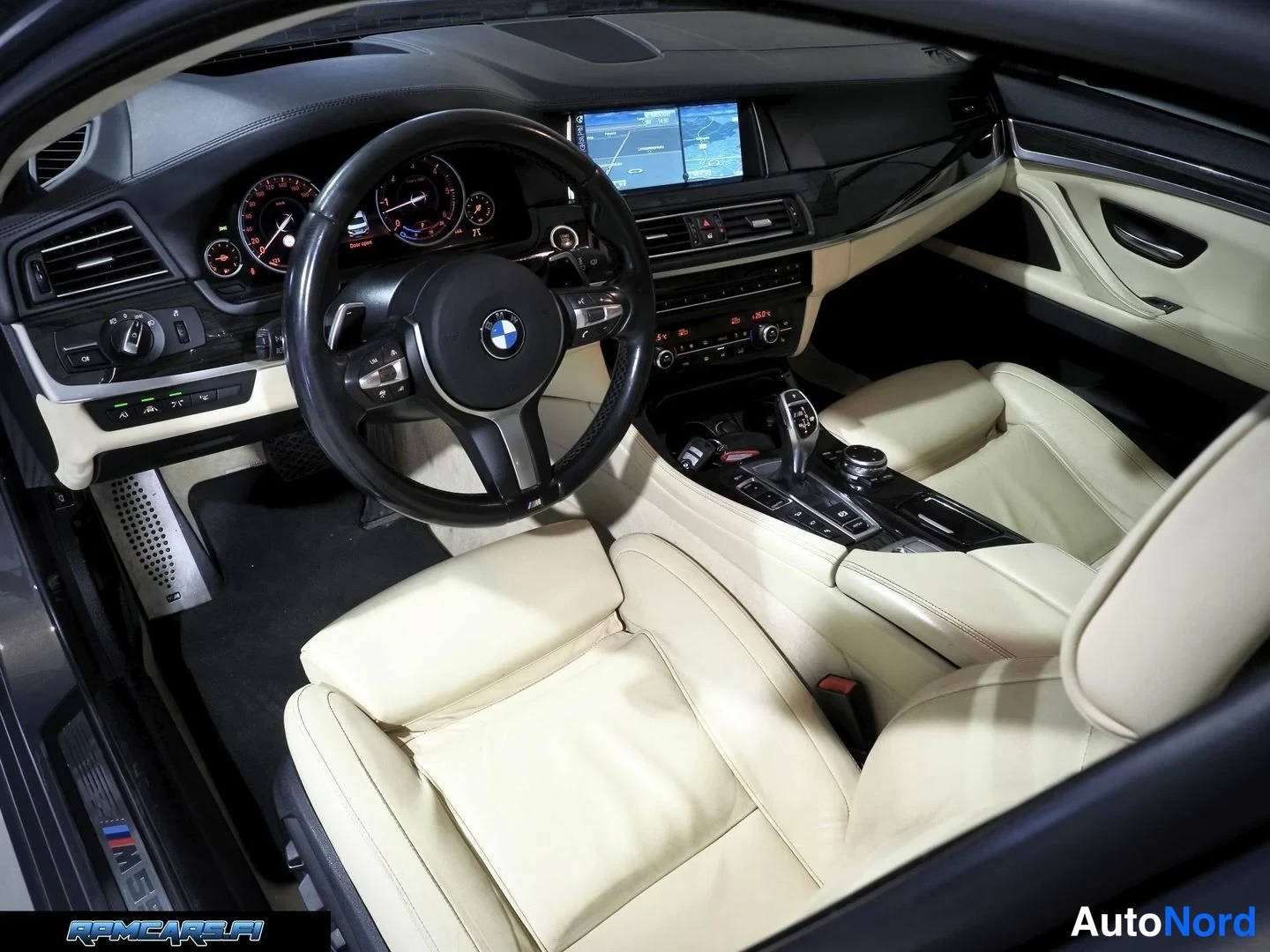 Muu: Auton sisätilat kuljettajan puolelta: musta BMW-ohjauspyörä, analogiset mittarit, keskikonsolilla näyttö ja kamerakuva, beige nahkapenkit.
