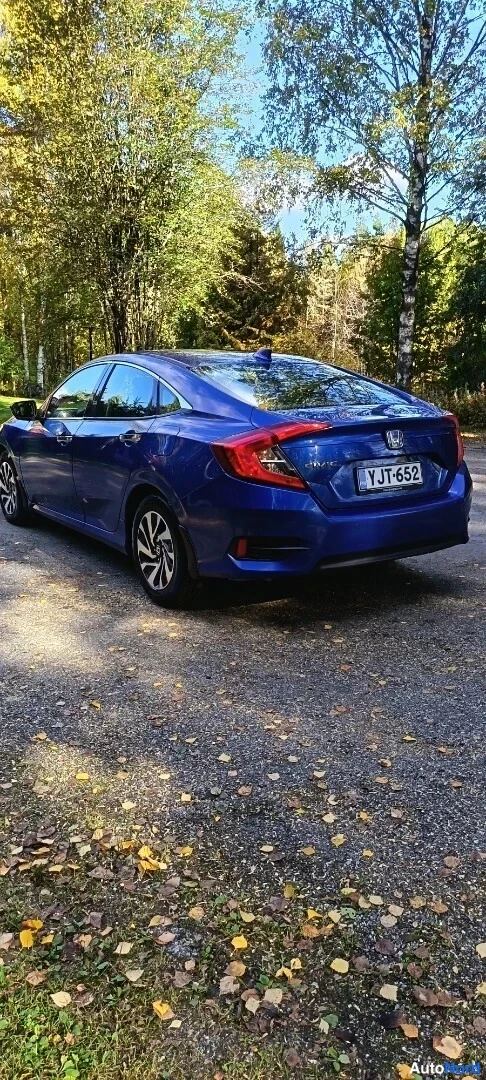 Takaviisto: Sininen Honda Civic -sedan takakulmasta vasemmalta, rekisteritunnus, syksyinen metsätie taustalla.