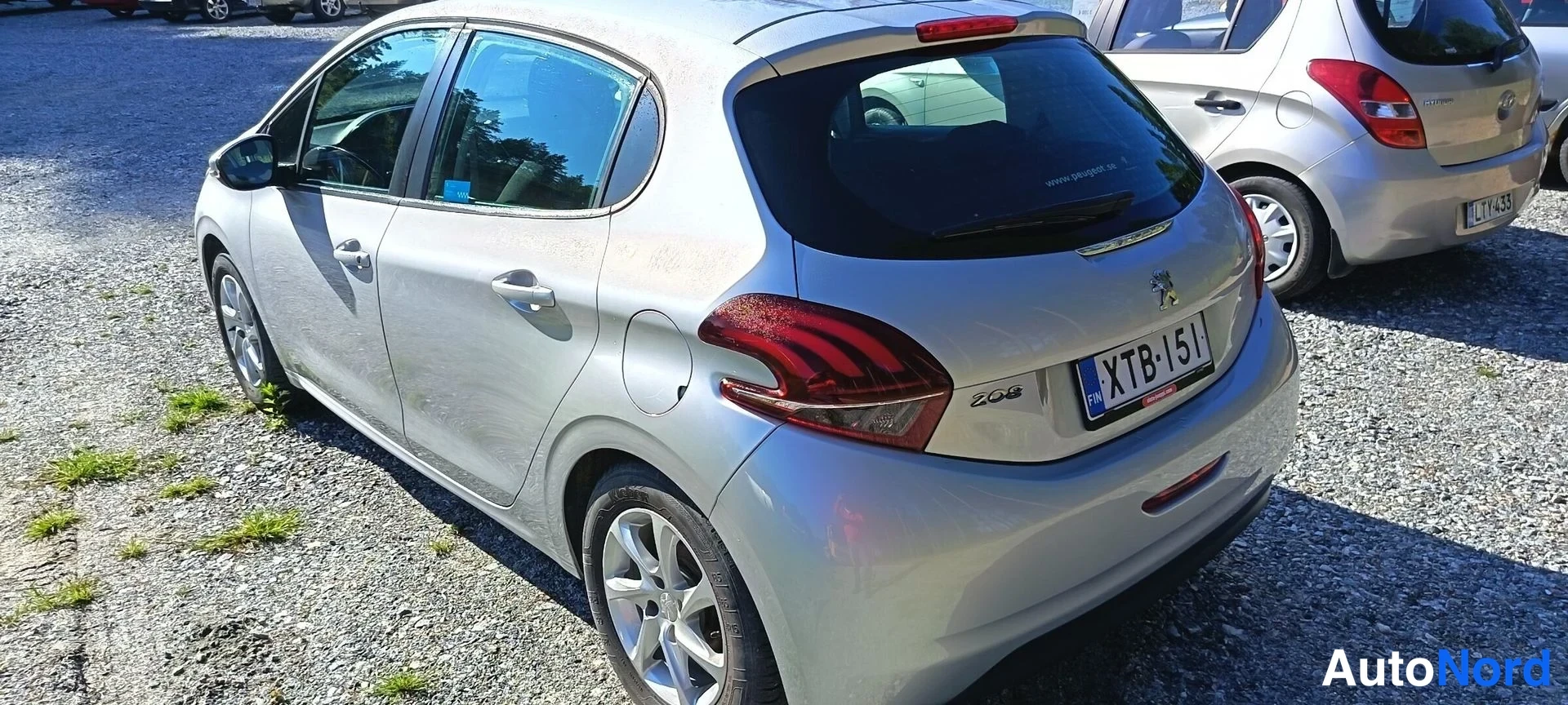 Takaviisto: Hopeanvärinen Peugeot 208 viistoperä takaa ja vasemmalta sivulta, rekisteritunnus, takapenkillä avattu ovi.