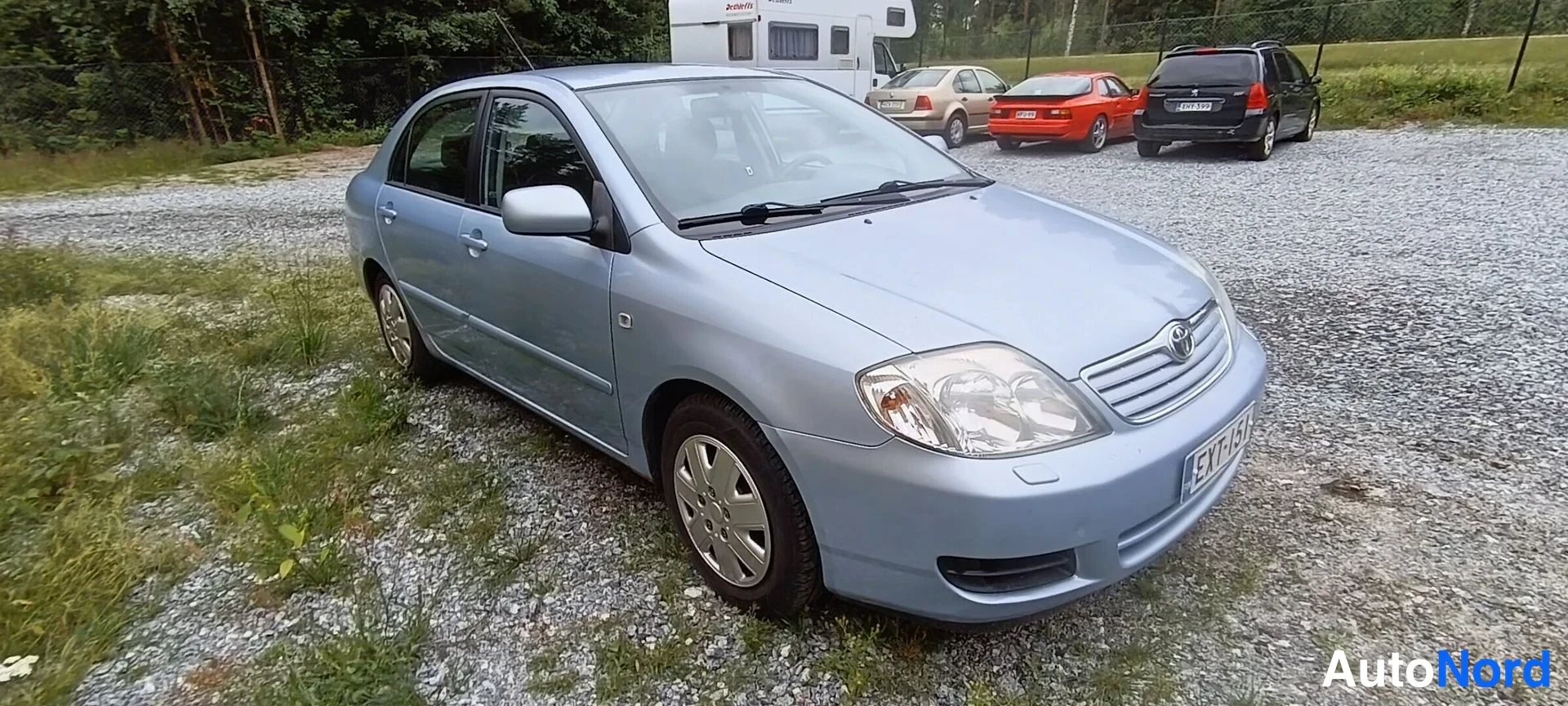 Etuviisto, nokka oikealle: Auton etukulma oikealta; etusäleikkö ja Toyota-merkki, ajovalot ja etupyörä näkyvät, rekisterikilpi lukee.